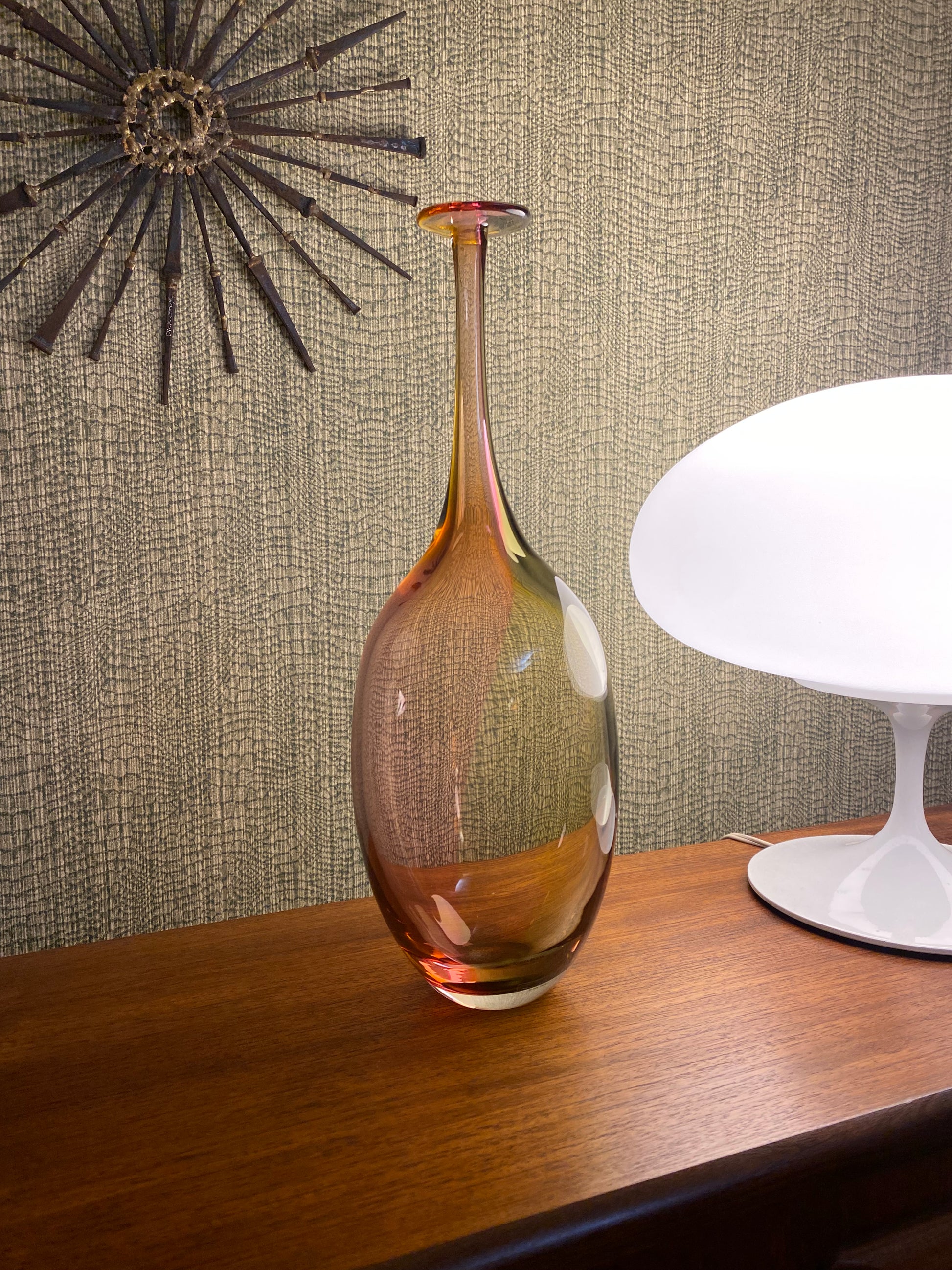 Decorative glass vase on a textured surface with a lamp in the background