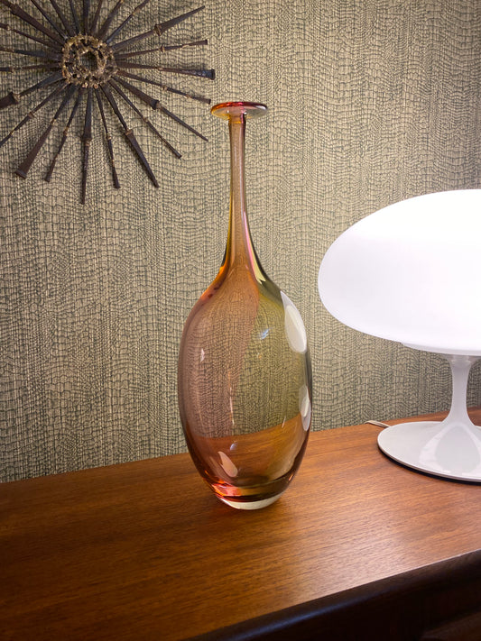 Decorative glass vase on a textured surface with a lamp in the background
