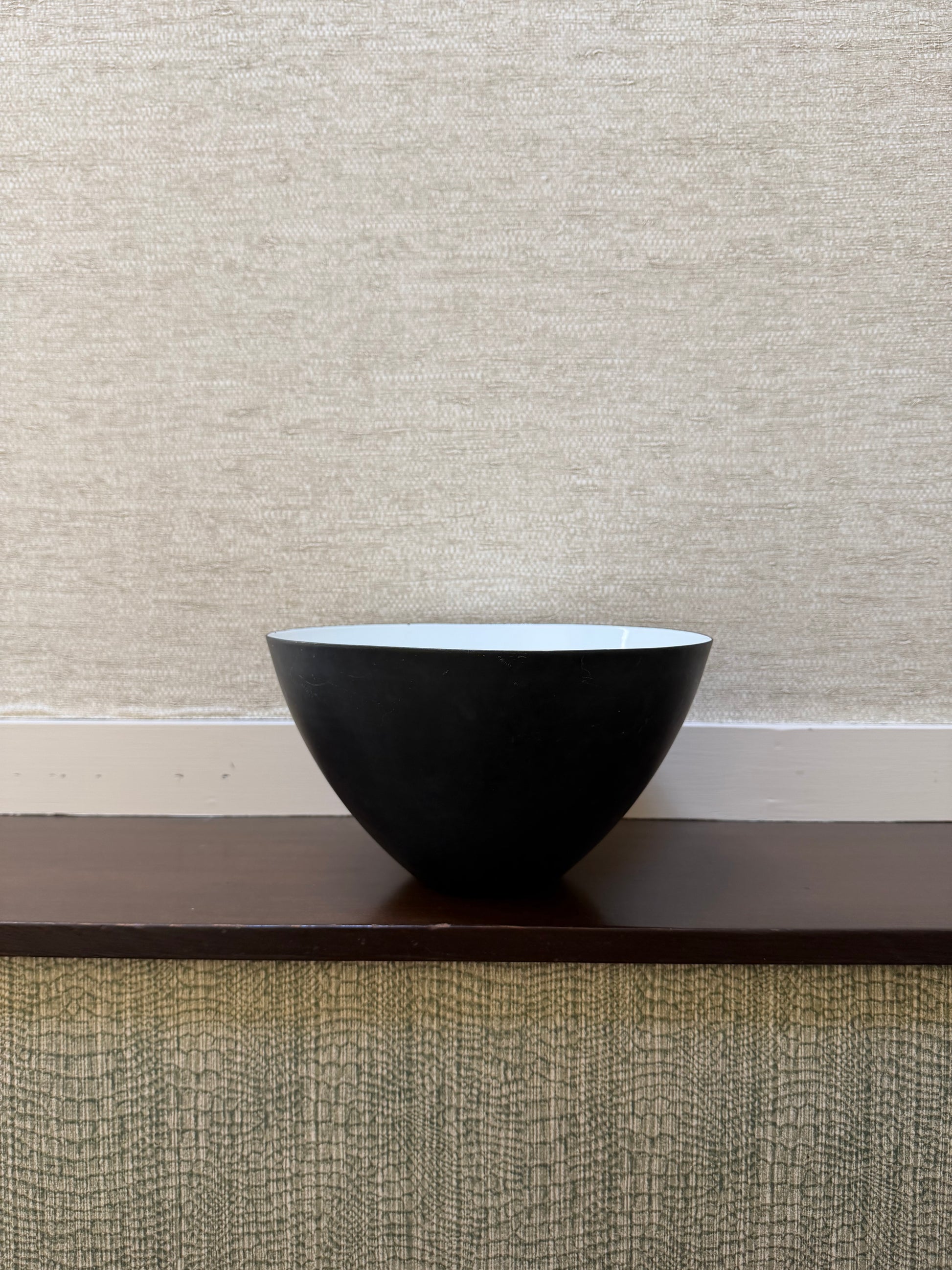 Black bowl on a wooden surface with a textured wall in the background