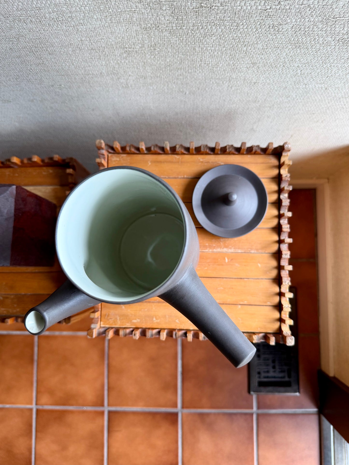 Green ceramic cup and black saucer on a wooden tray with a textured wall background