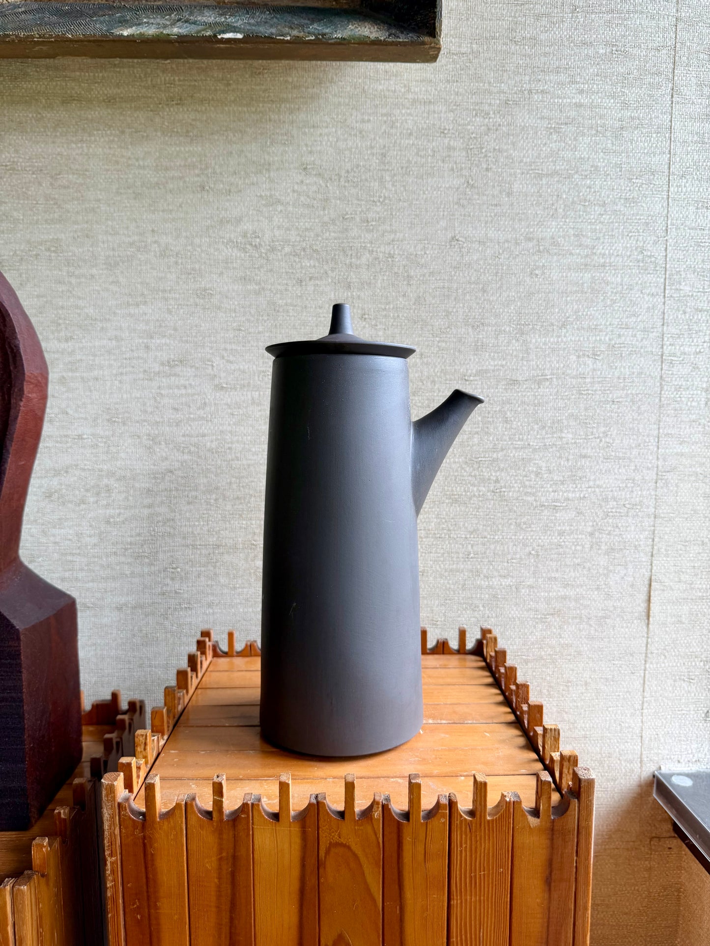 Gray teapot on a wooden stand against a beige wall