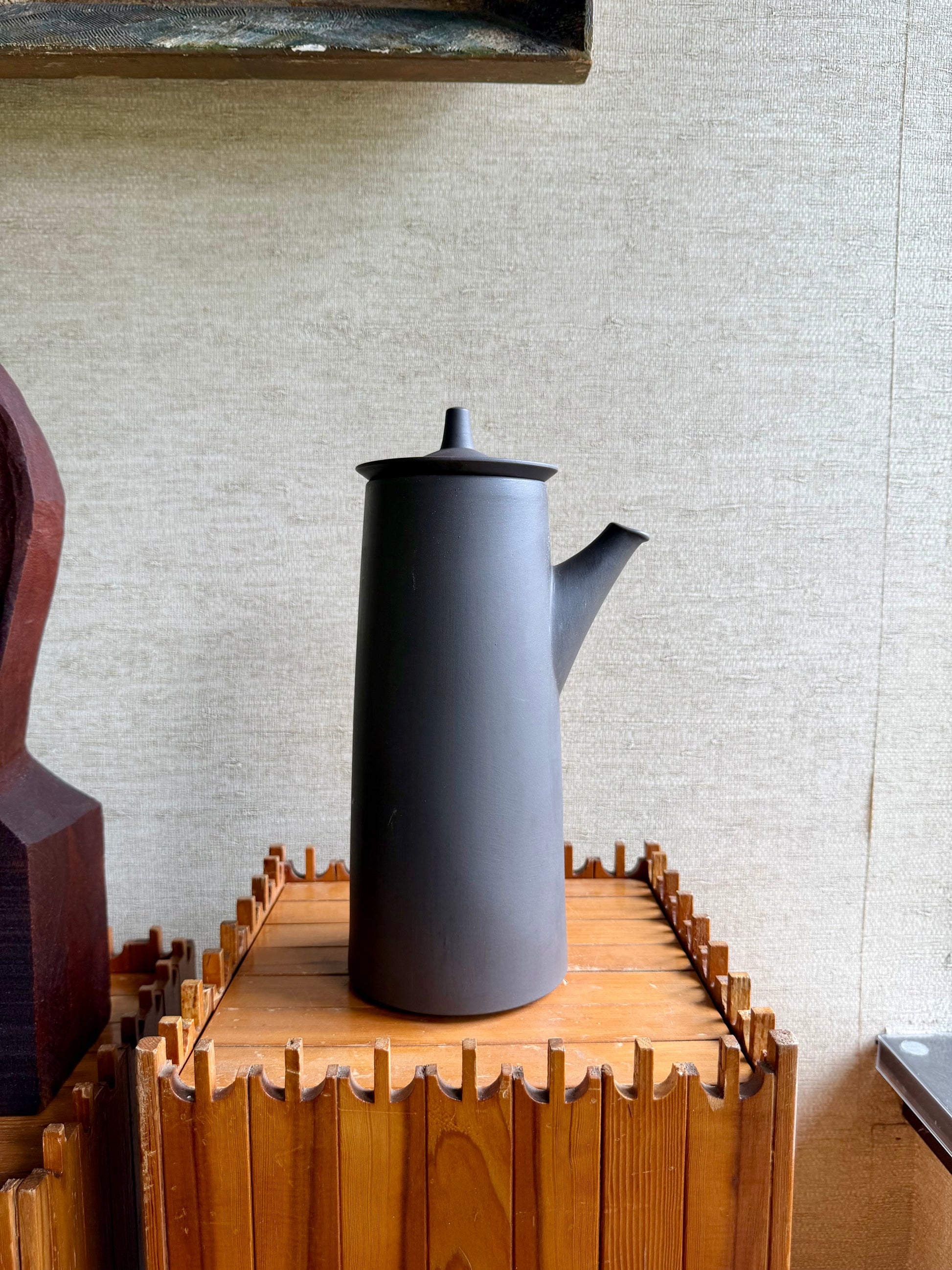 Gray teapot on a wooden stand against a beige wall