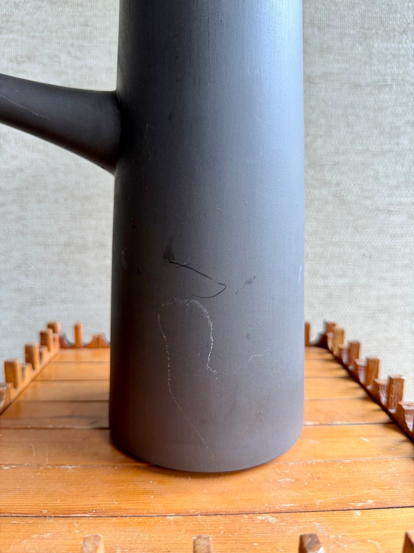 Close-up of a dark gray pitcher on a wooden surface with a light gray background