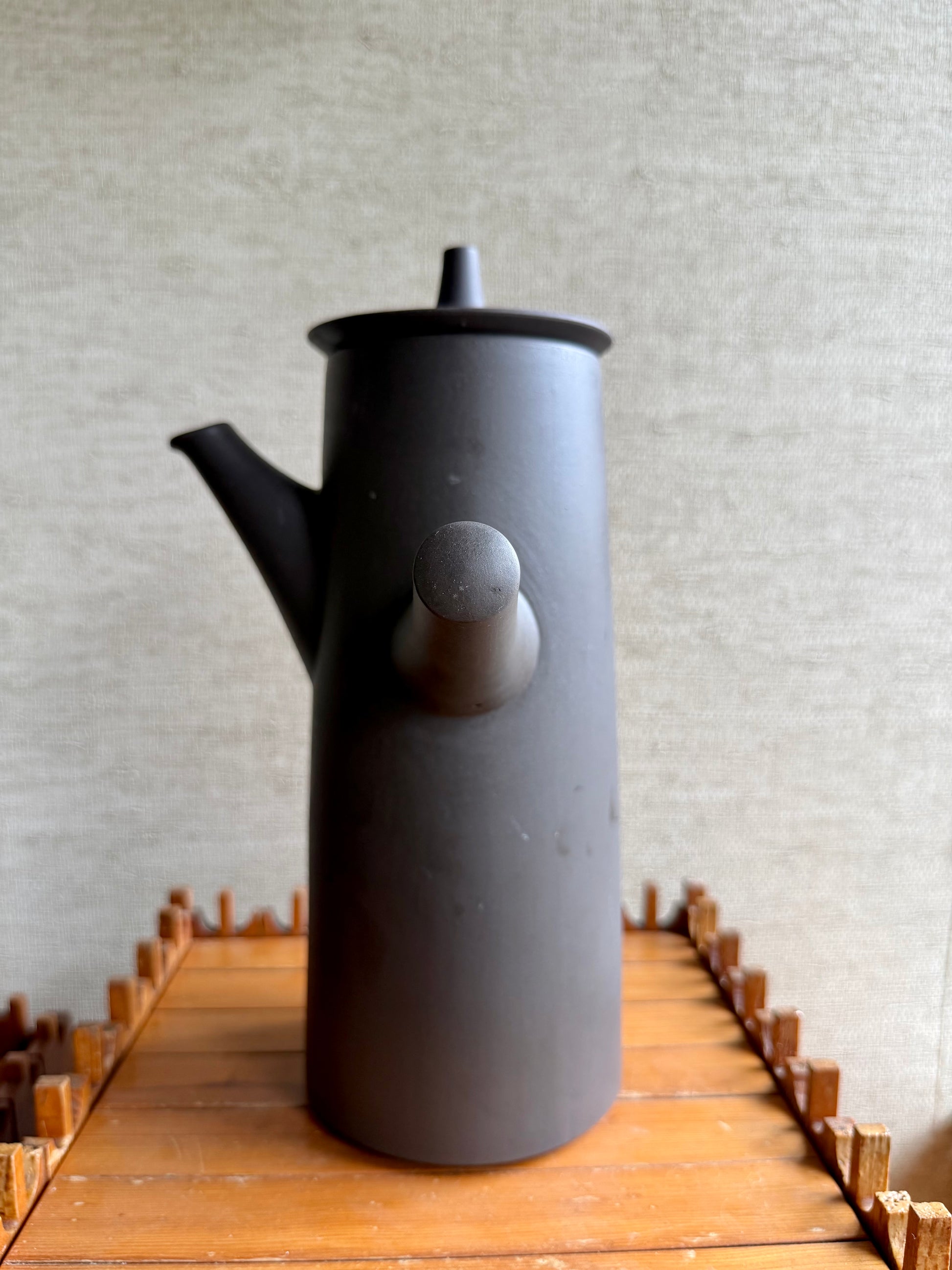 Black ceramic teapot on a wooden surface with a textured gray wall background