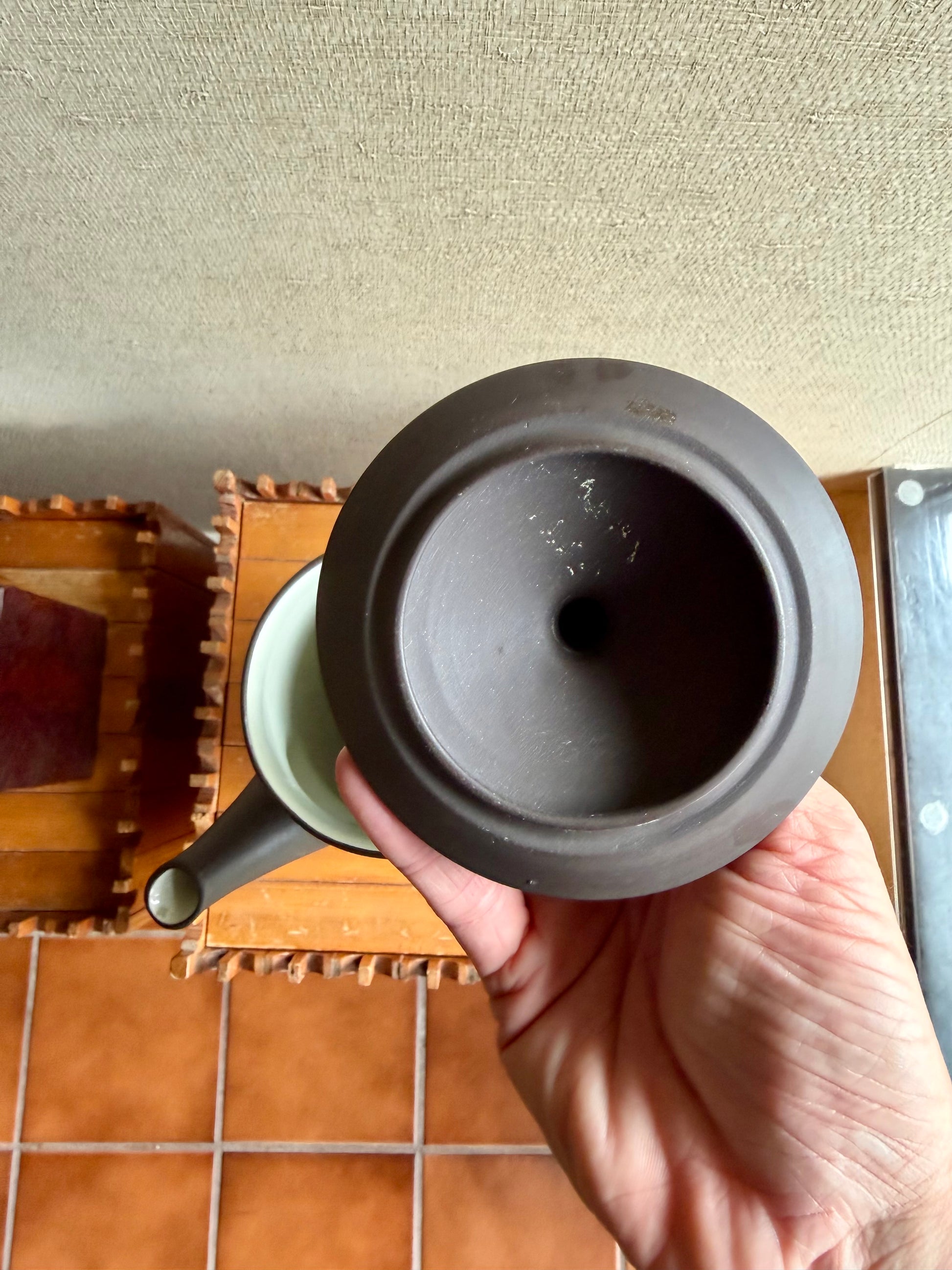 Hand holding a ceramic teapot with a wooden tray in the background