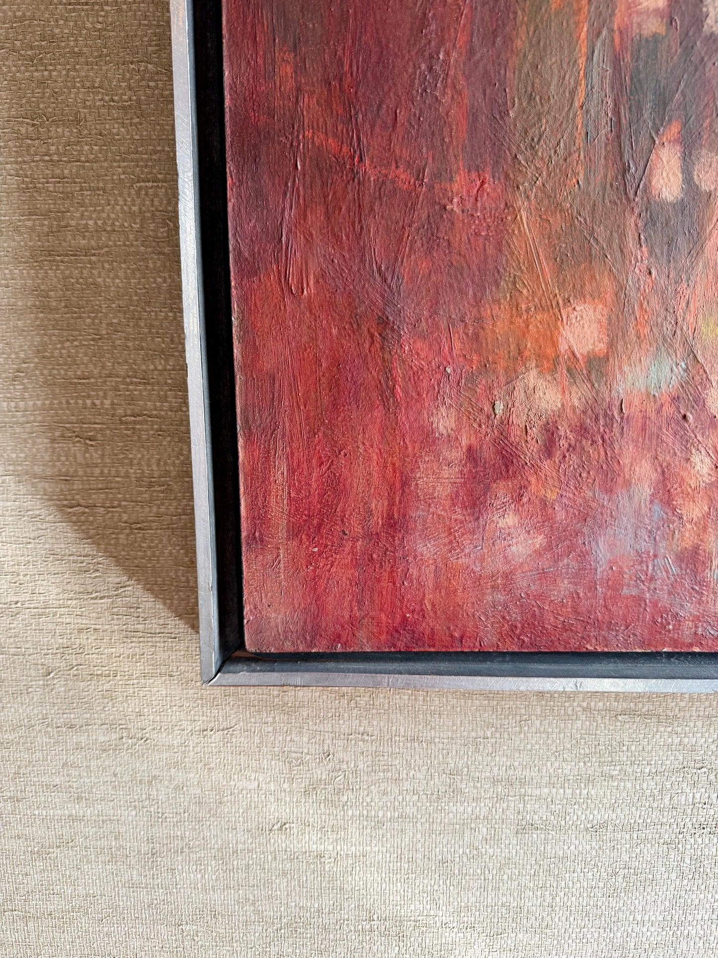 Close-up of a textured red painting with a black frame on a beige surface.