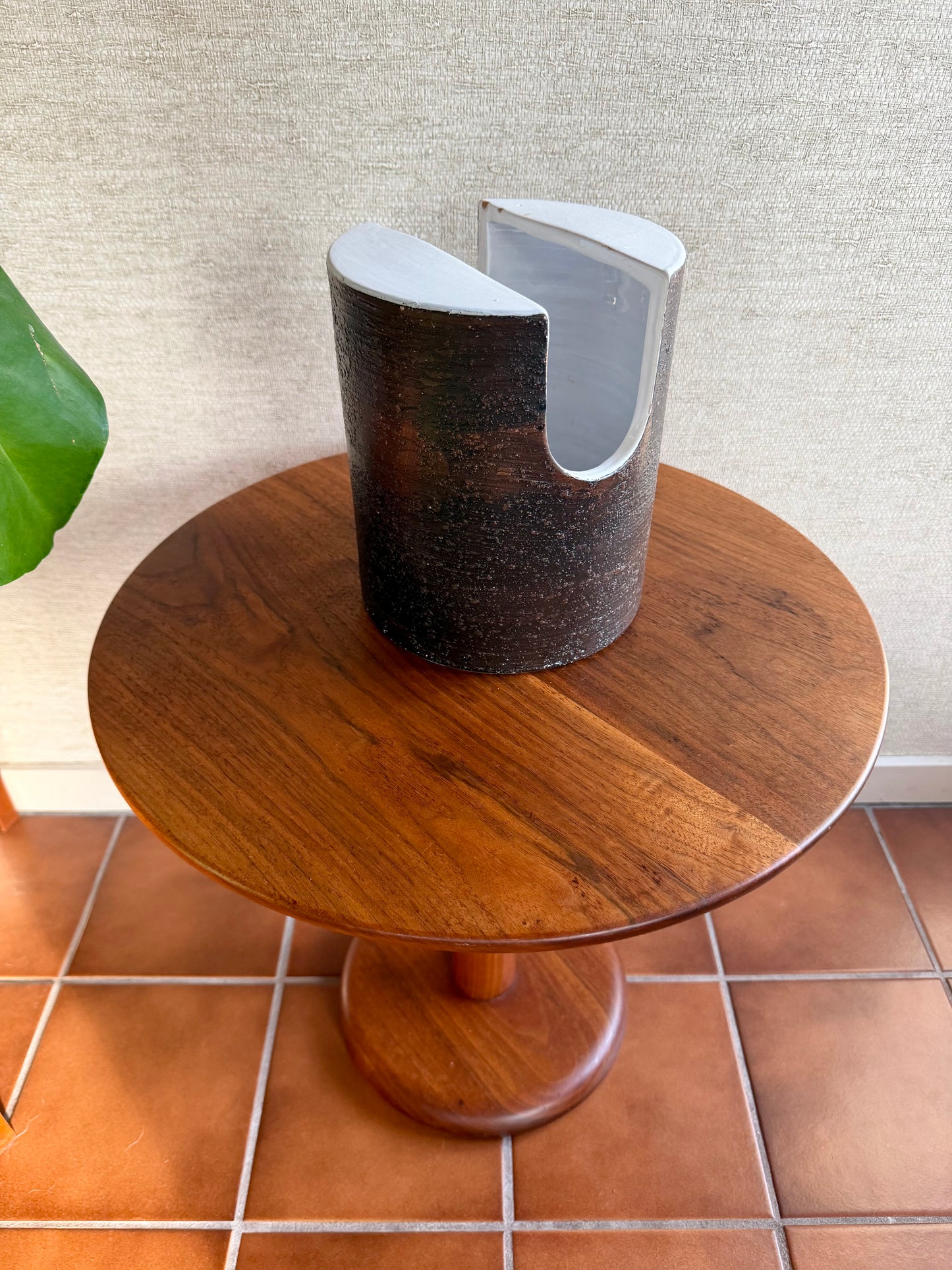 Round wooden table with a cylindrical object on top against a textured wall.