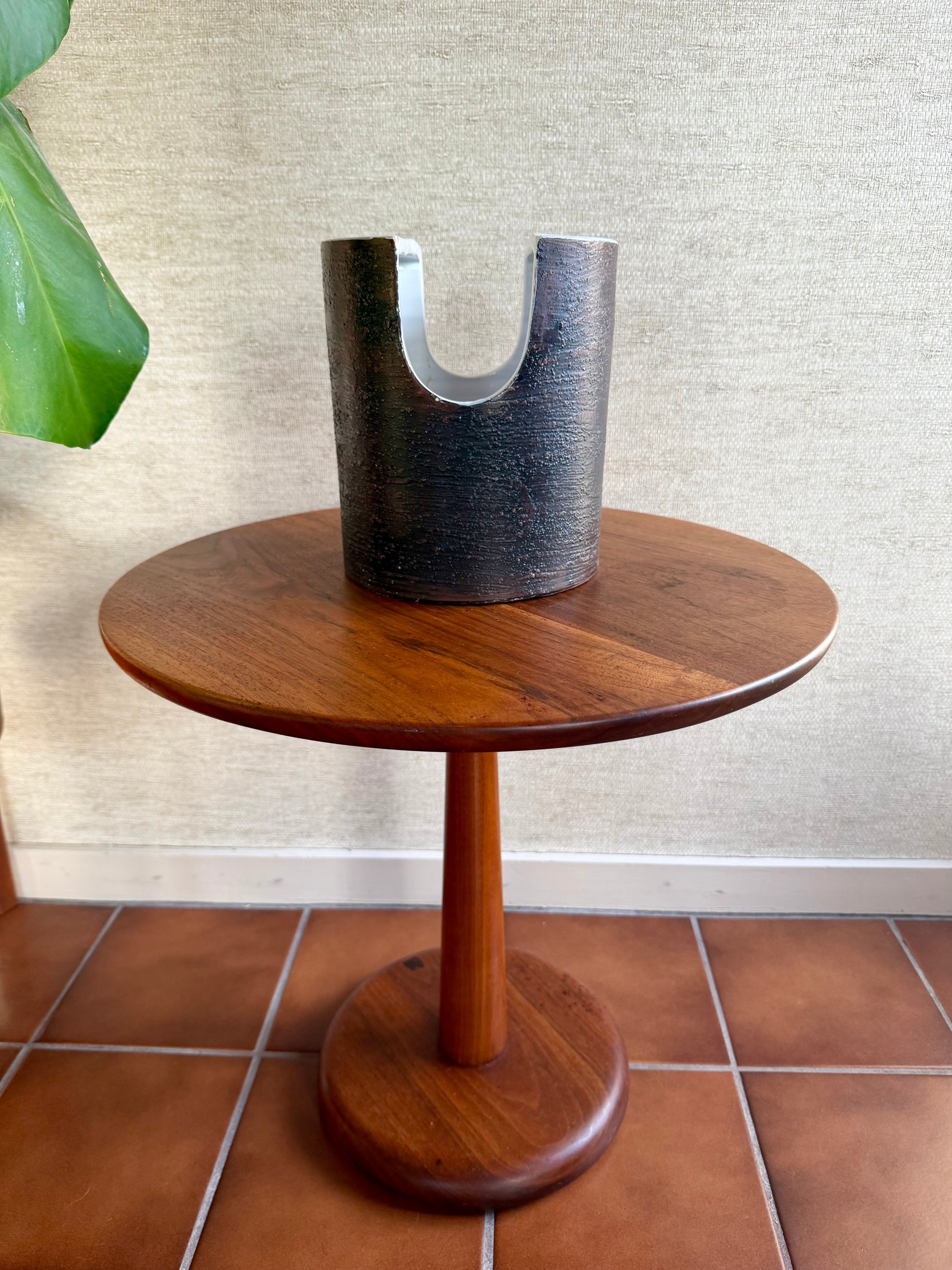 Wooden side table with a cylindrical metal vase on a textured wall background