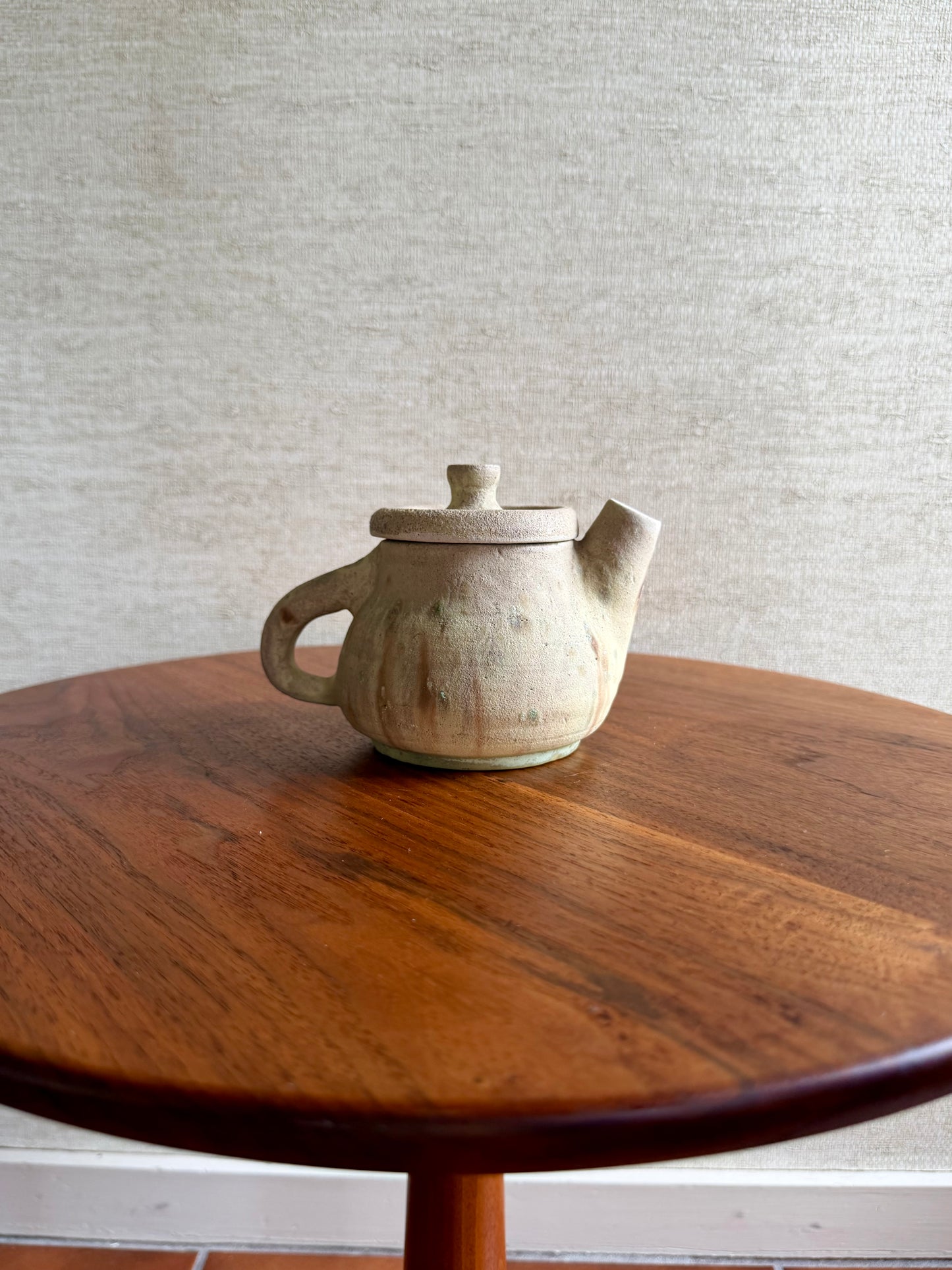 Ceramic teapot on a wooden table with a textured wall background