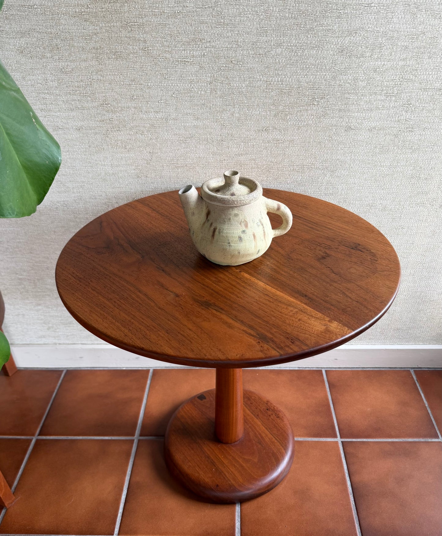 Wooden side table with a ceramic teapot on a tiled floor and light gray wall background