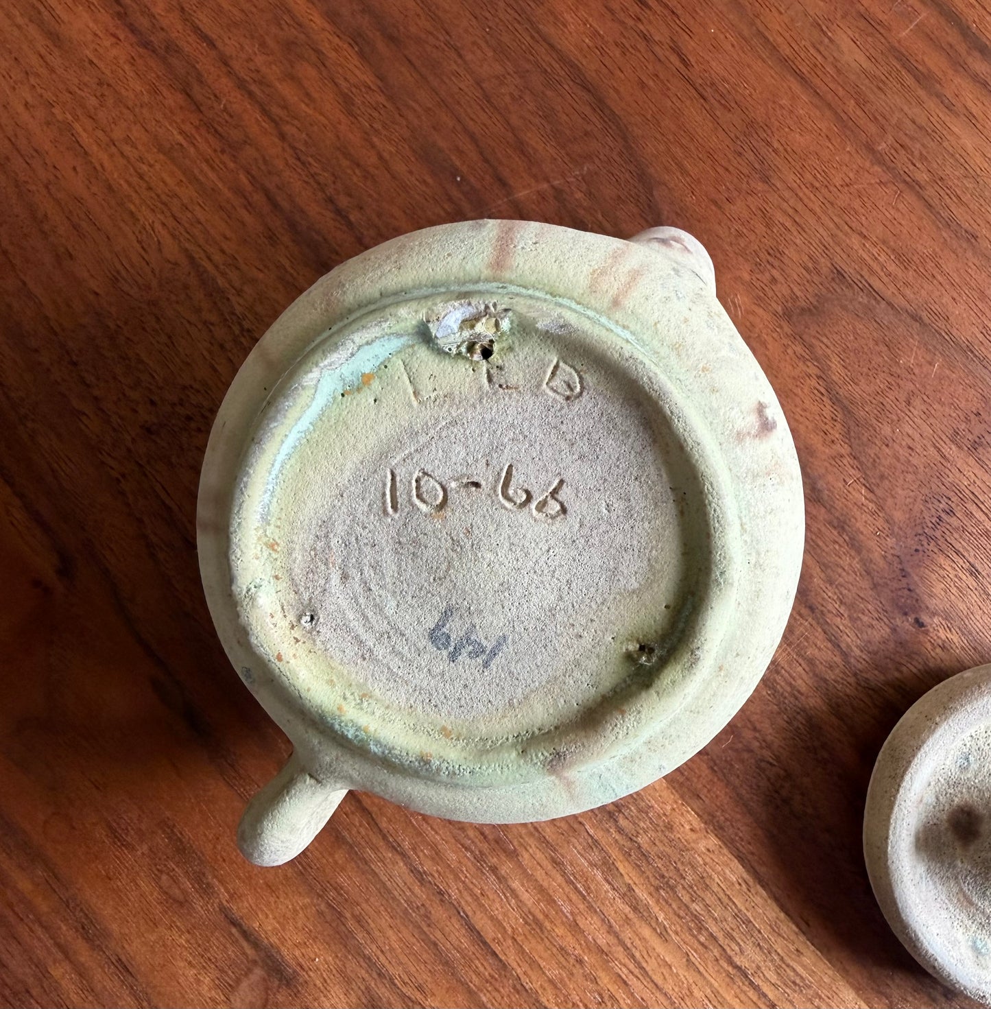 Ceramic teapot lid with 'LTD' and '10-66' branding on a wooden surface