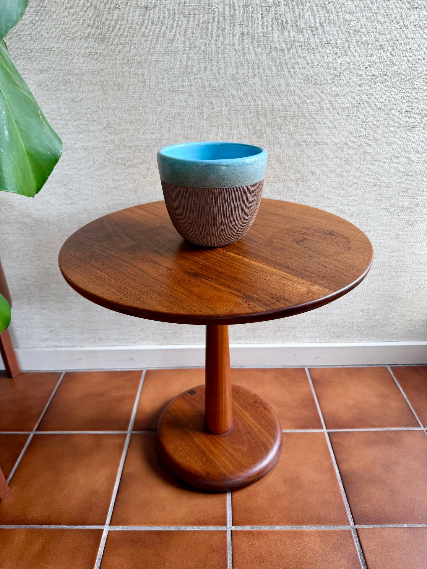 Wooden side table with a blue and brown ceramic cup on a tiled floor.