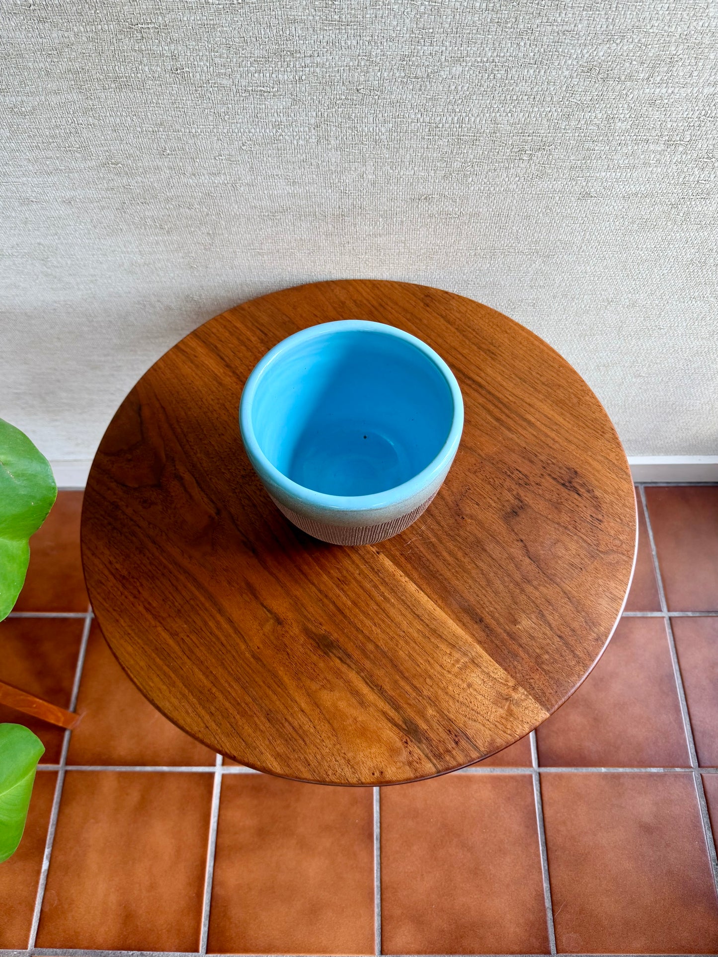 Blue ceramic cup on a wooden table with a tiled floor and textured wall in the background