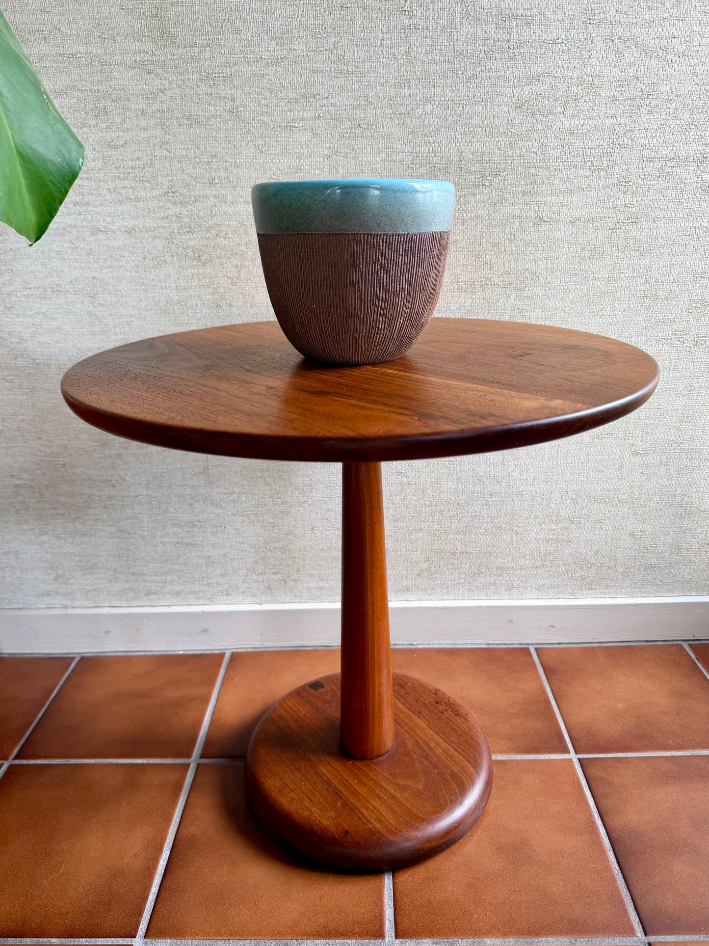 Wooden side table with a ceramic bowl on a tiled floor against a textured wall.