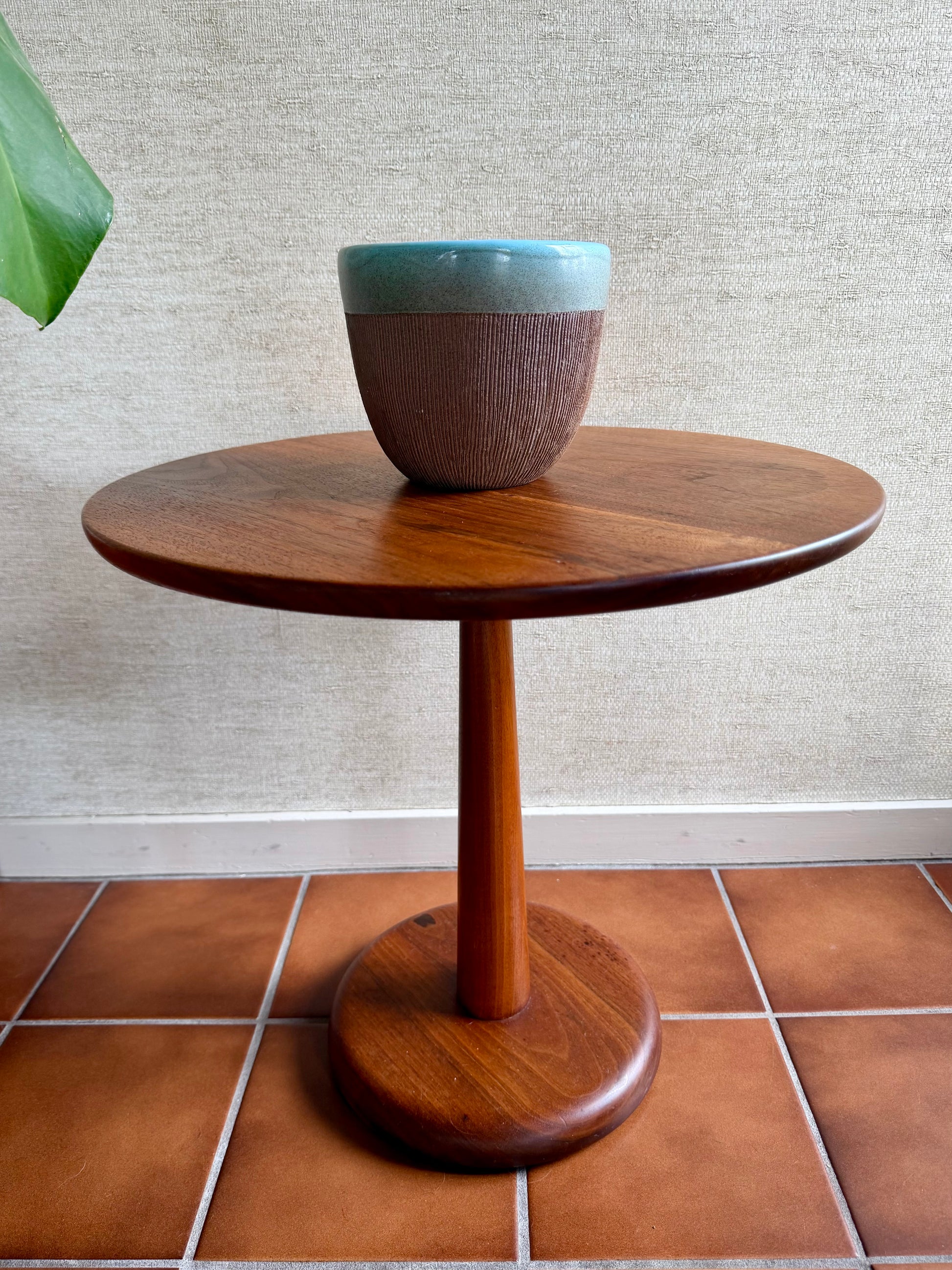 Wooden side table with a ceramic bowl on a tiled floor against a textured wall.