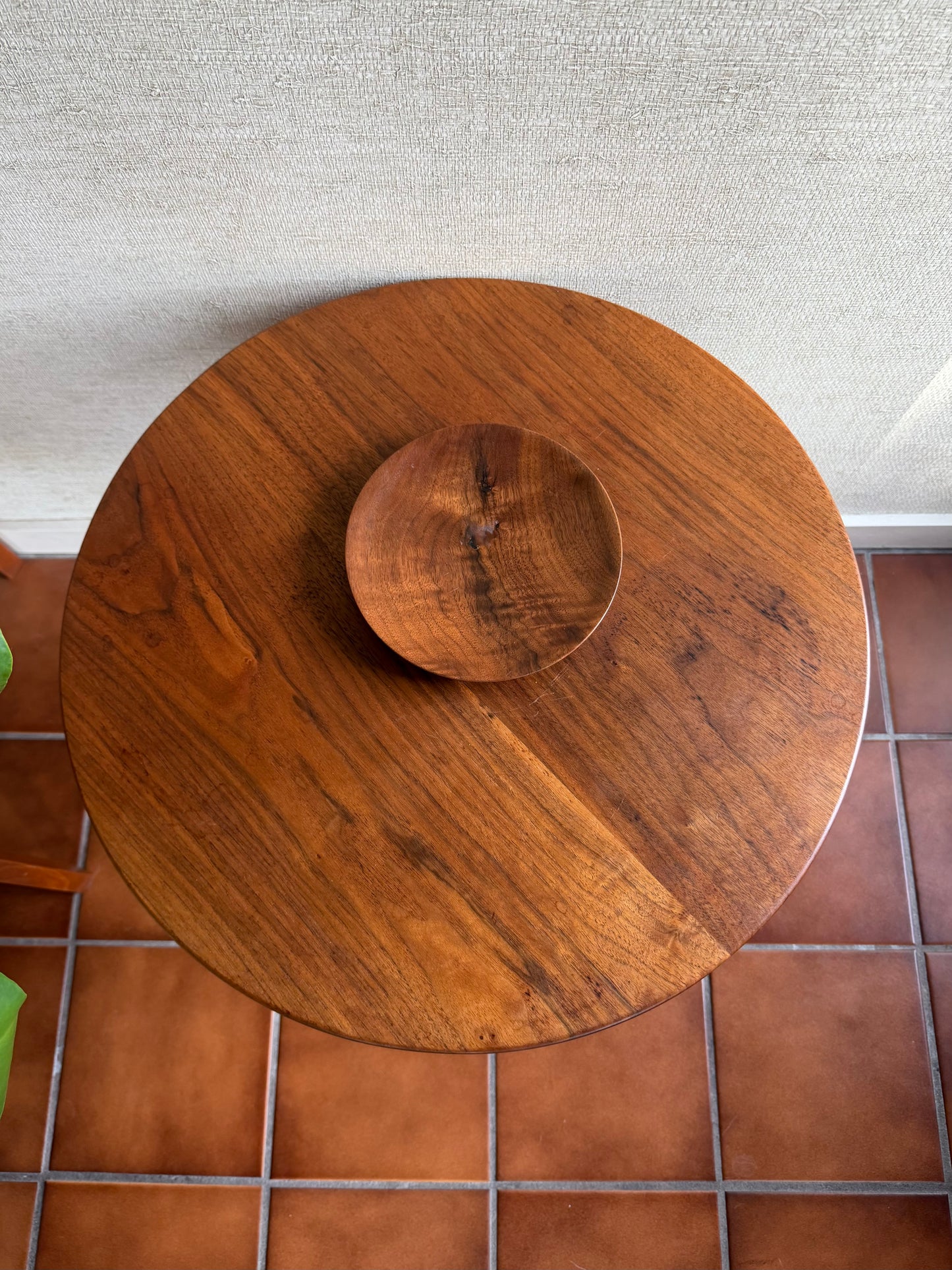 Wooden round table with a matching bowl on a tiled floor.