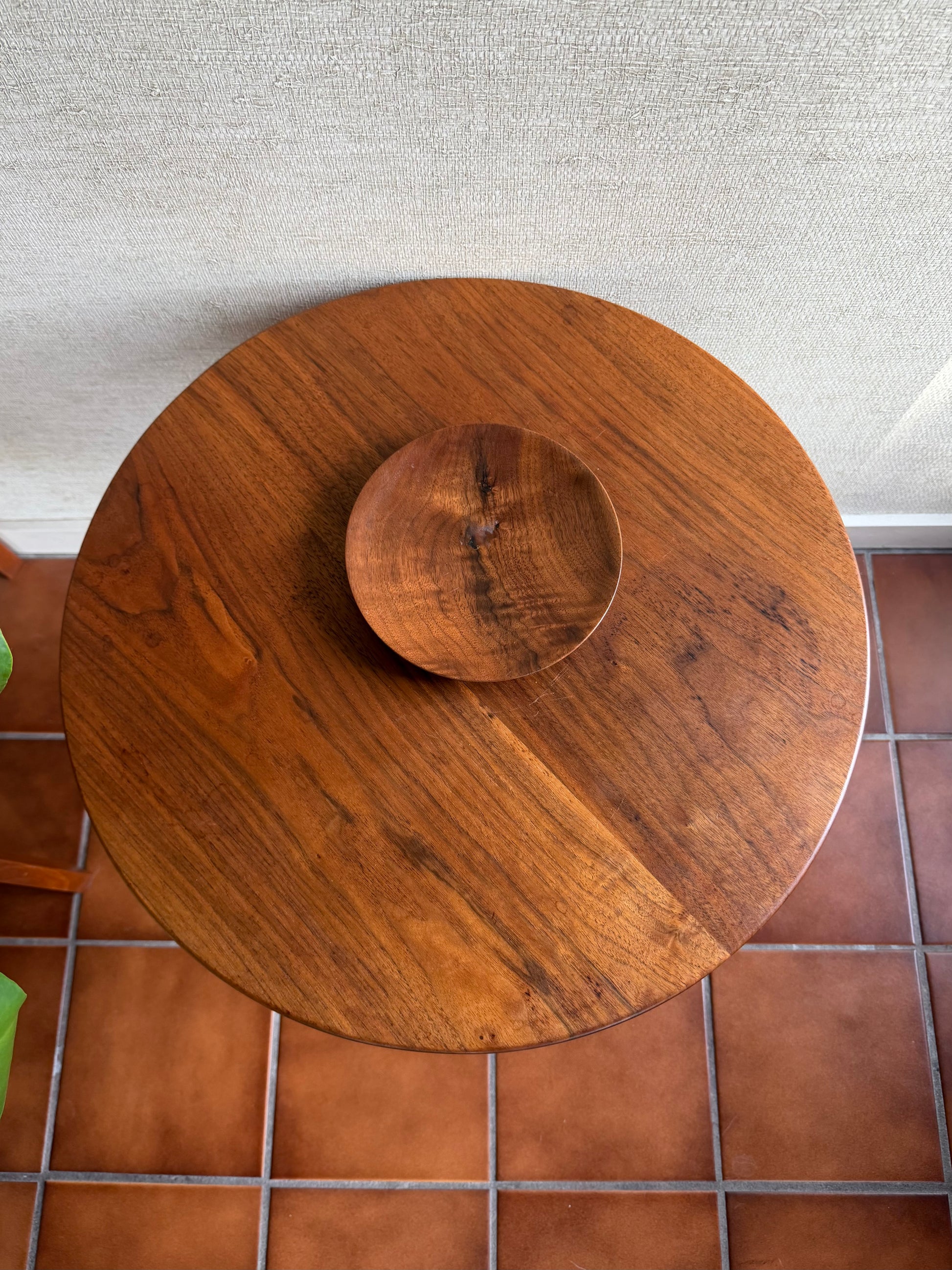 Wooden round table with a matching bowl on a tiled floor.