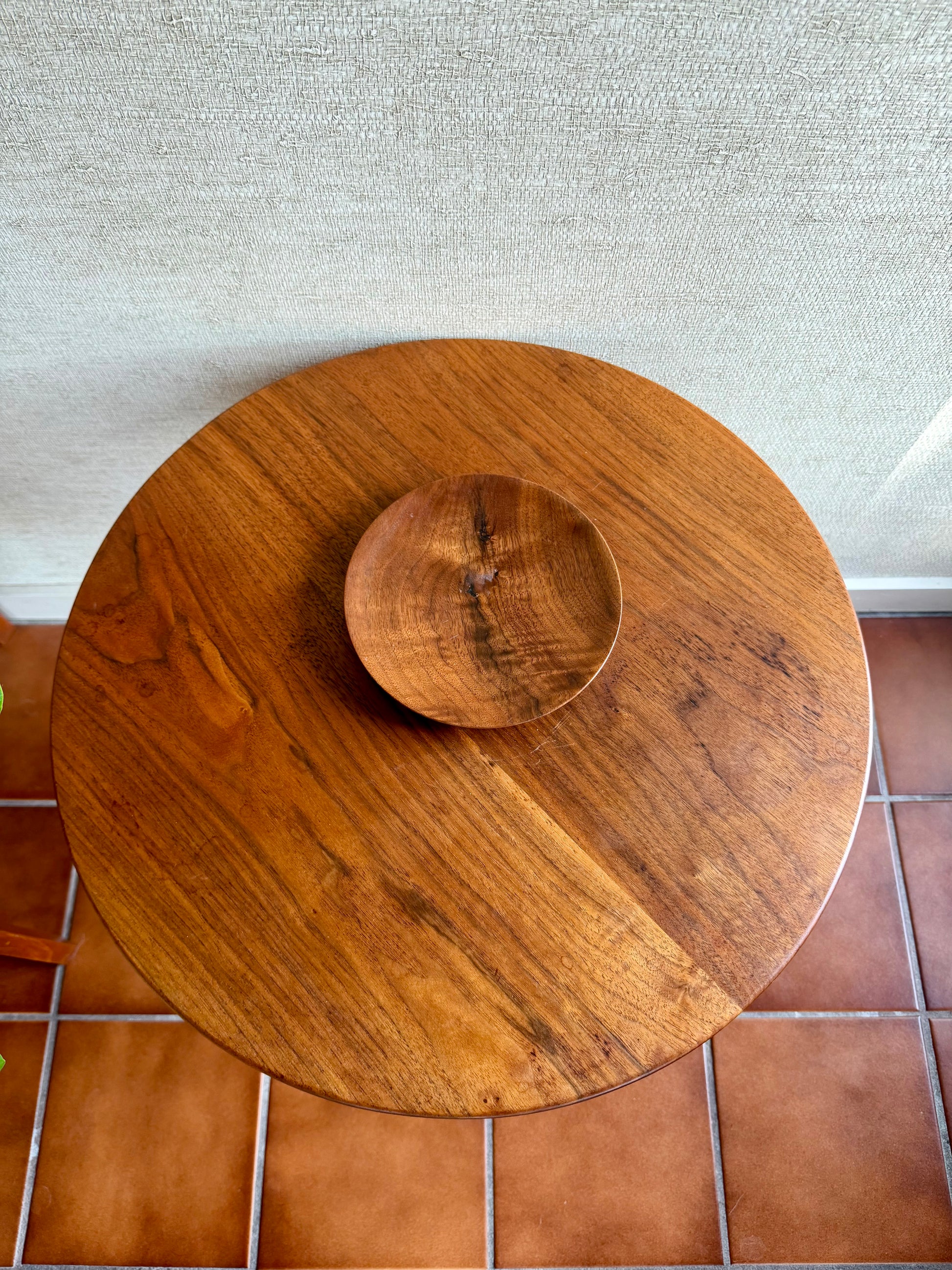 Wooden round table with a matching bowl on a tiled floor.