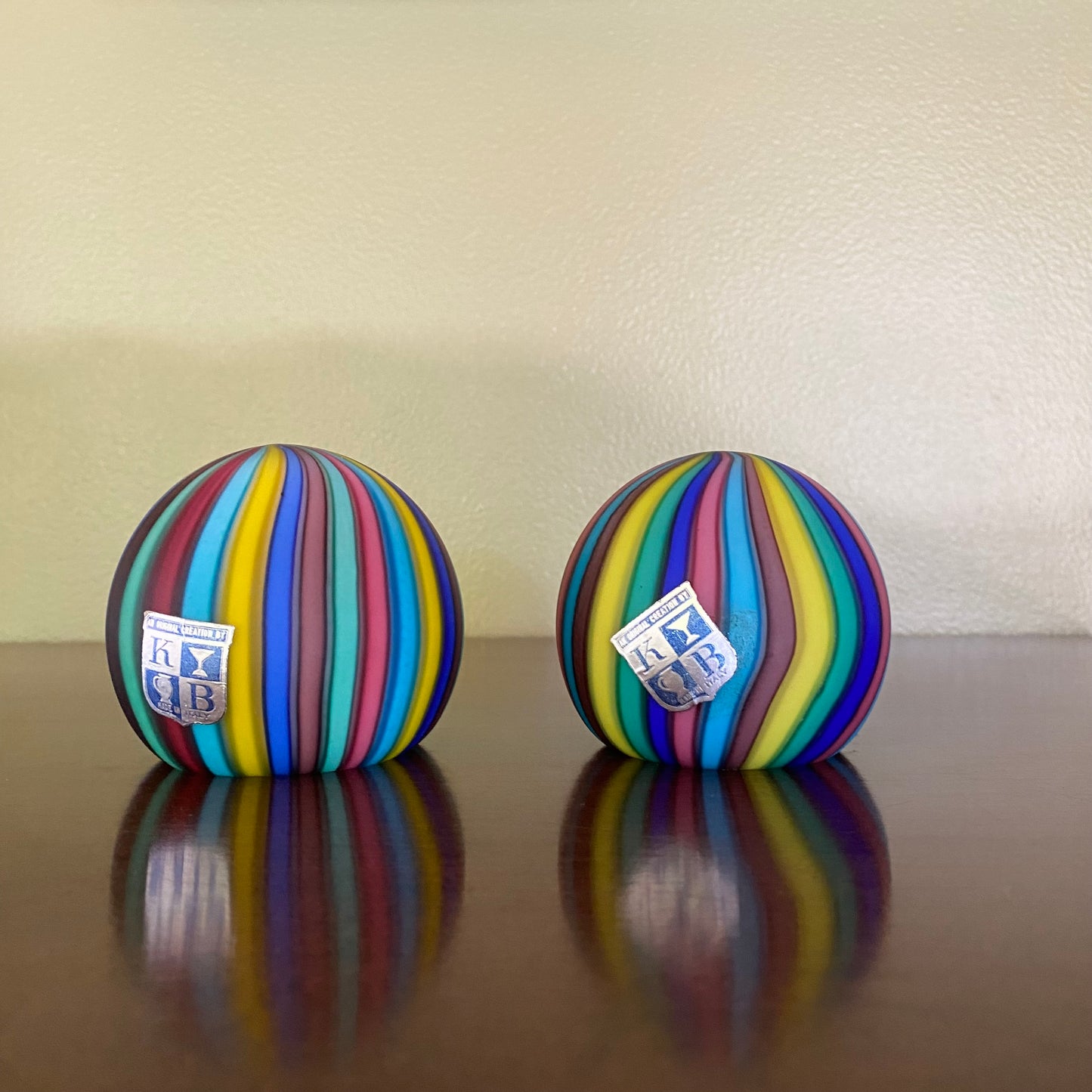 Two colorful striped balls with a logo on a reflective surface and beige background
