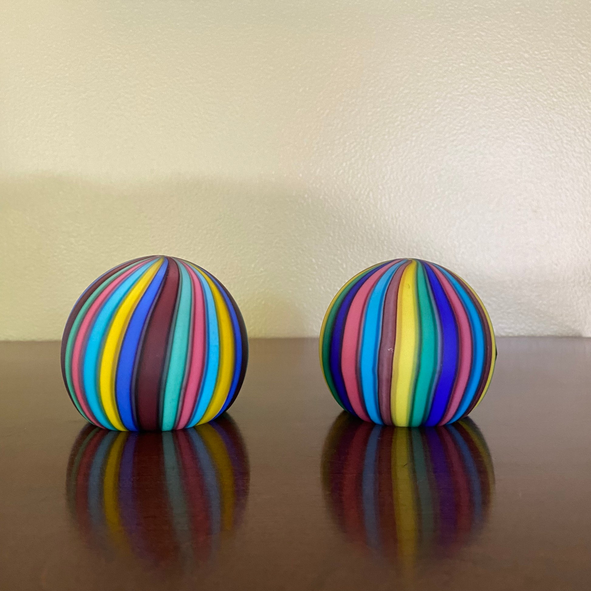 Two colorful striped balls on a reflective surface with a neutral background