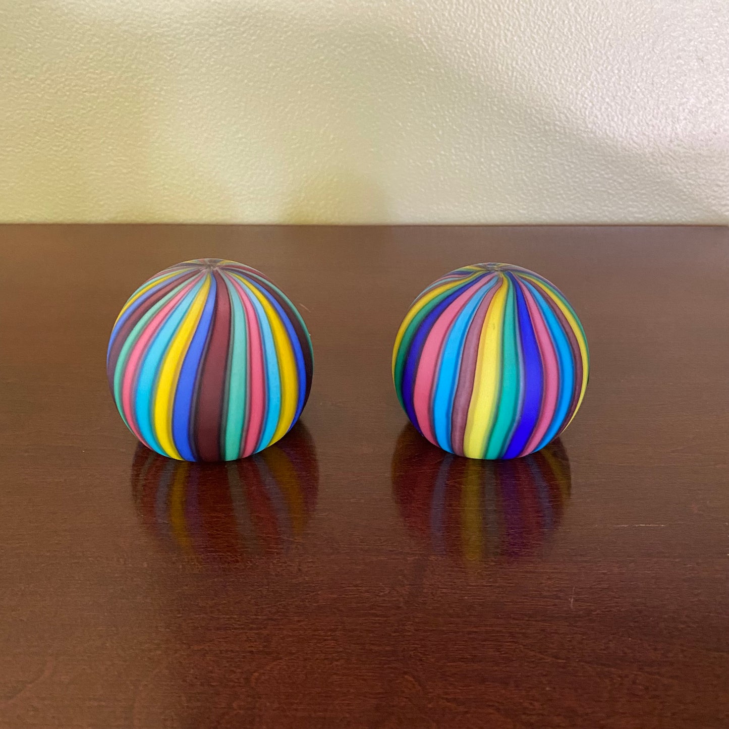 Two colorful striped balls on a wooden surface with a white wall background