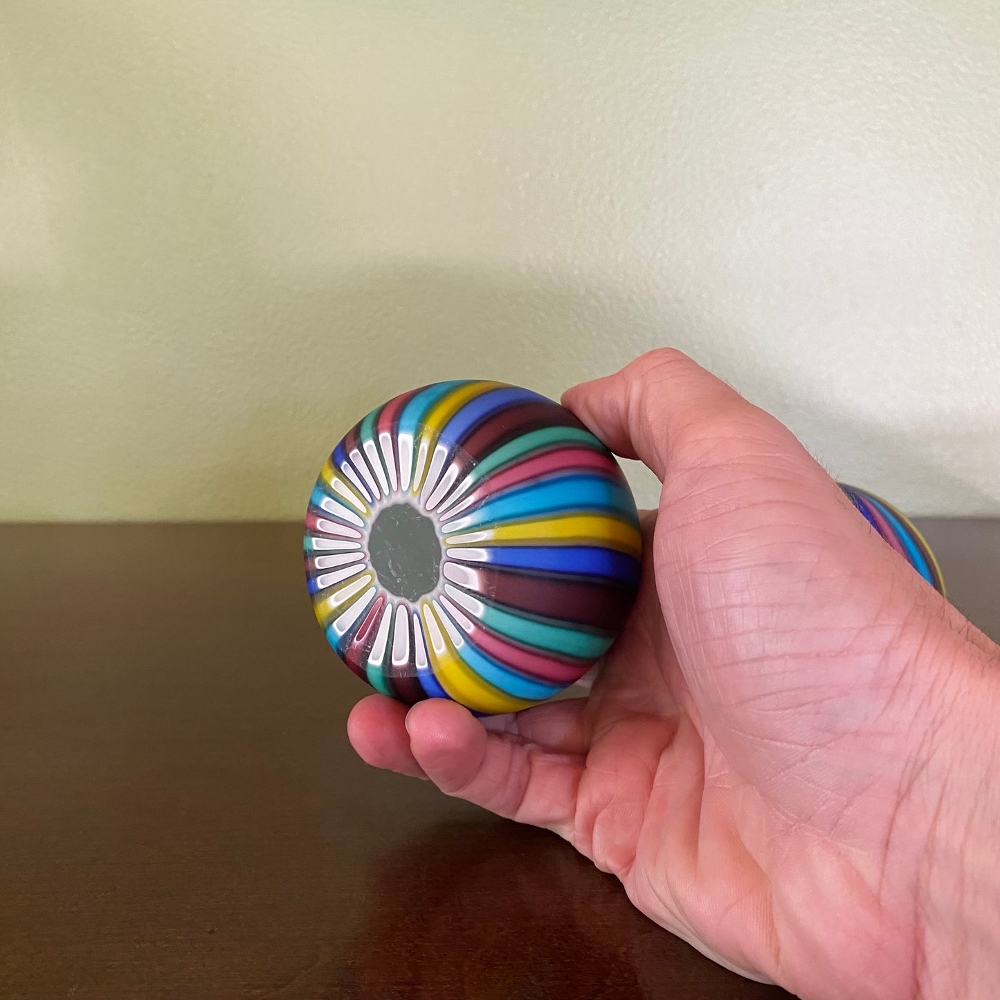 Hand holding a colorful striped ball against a neutral background