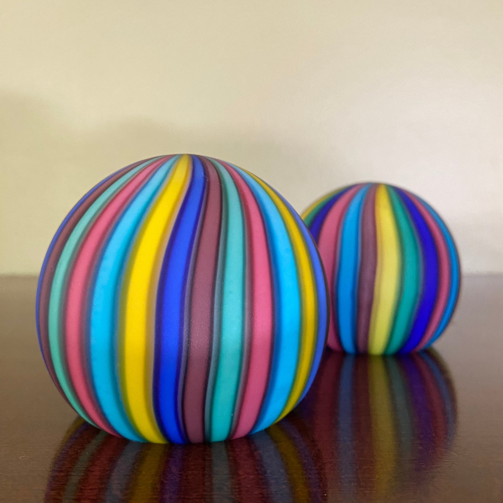 Two colorful striped balls on a reflective surface with a neutral background