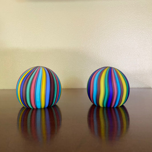 Two colorful striped balls on a reflective surface with a neutral background