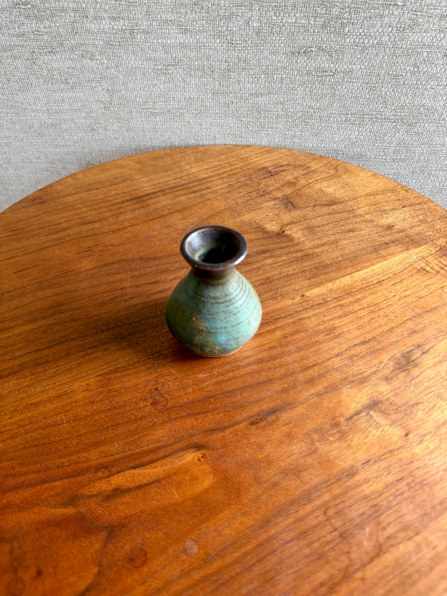 Small green ceramic vase on a wooden surface with a gray textured background