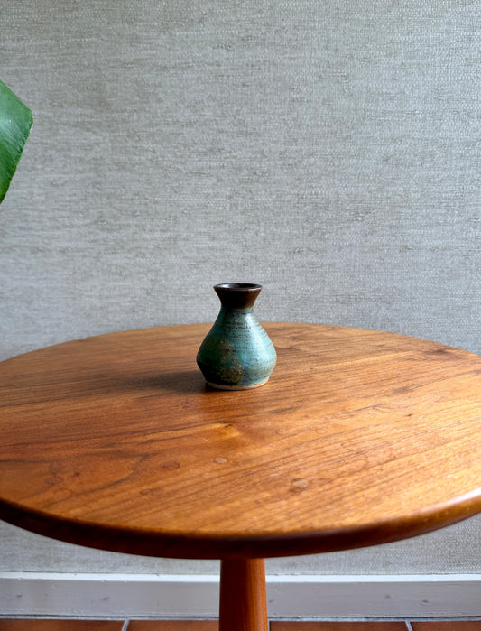 Small green ceramic vase on a wooden table against a gray wall.