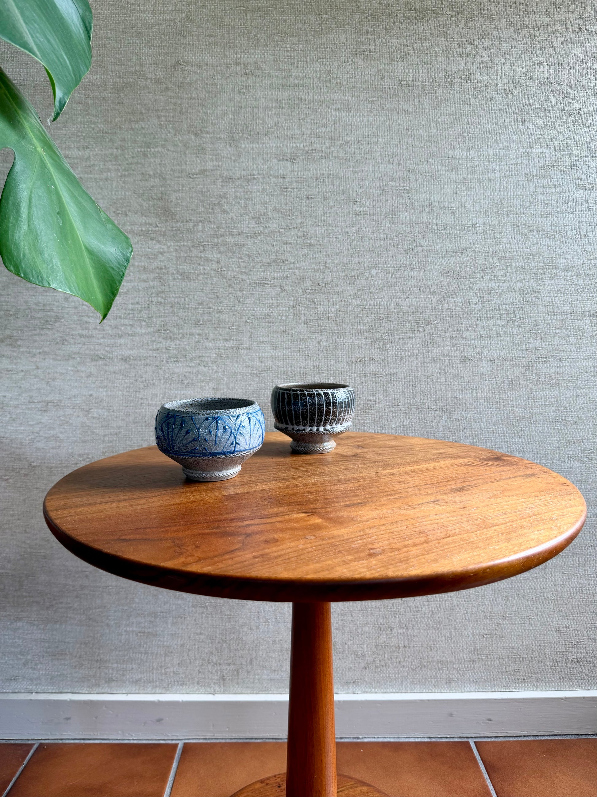 Round wooden table with two ceramic bowls on a textured wall background
