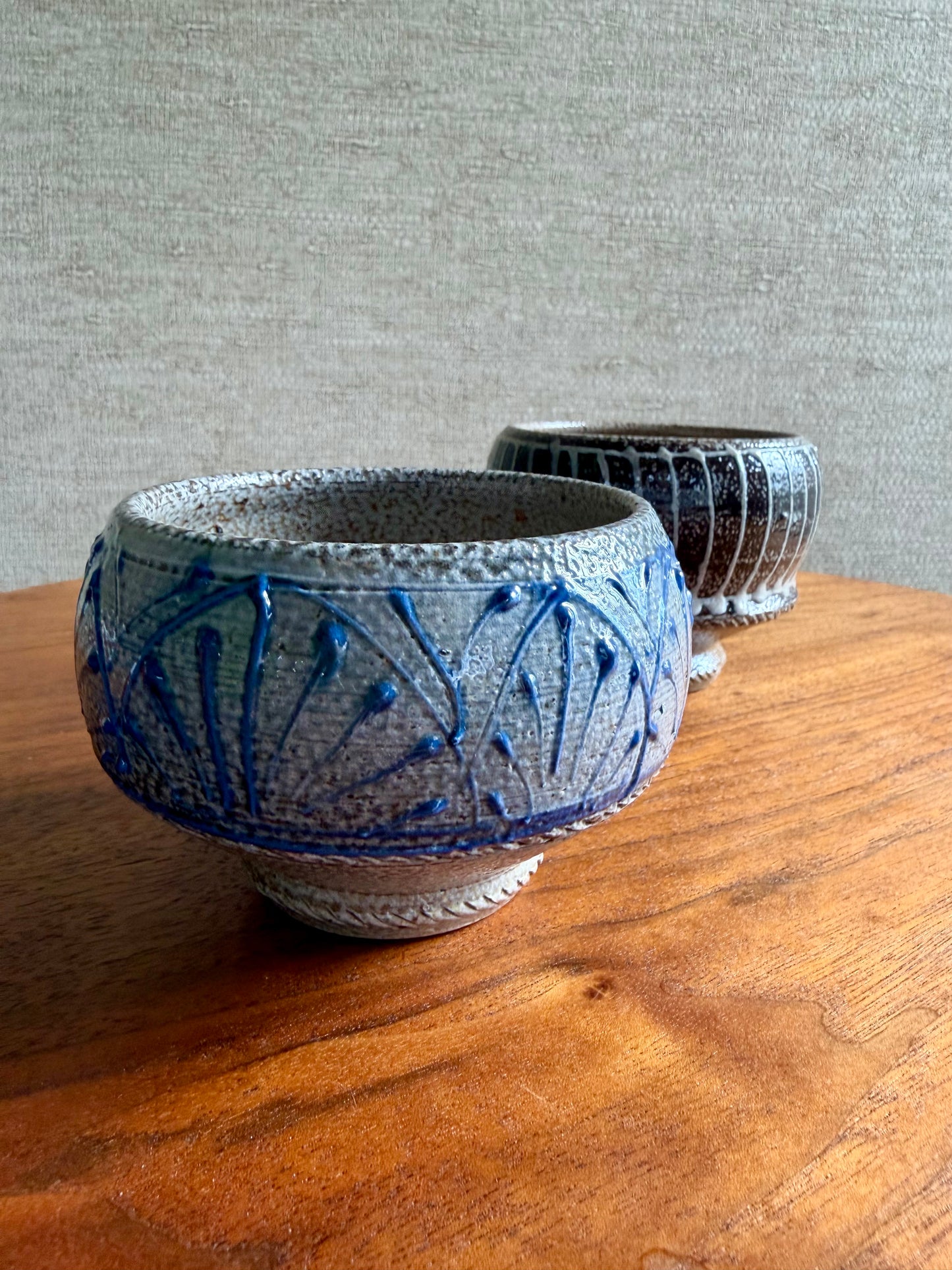 Two ceramic bowls with blue patterns on a wooden surface against a gray wall.