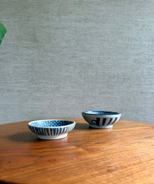 Two small ceramic bowls with blue patterns on a wooden surface against a gray wall.