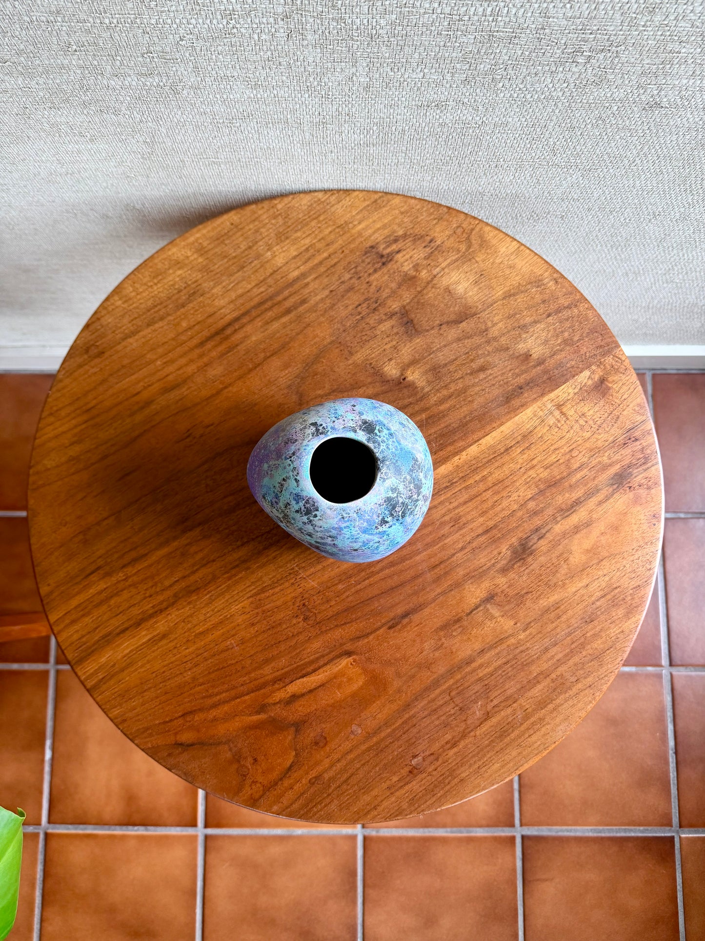 Small ceramic vase on a wooden stool with a tiled floor background