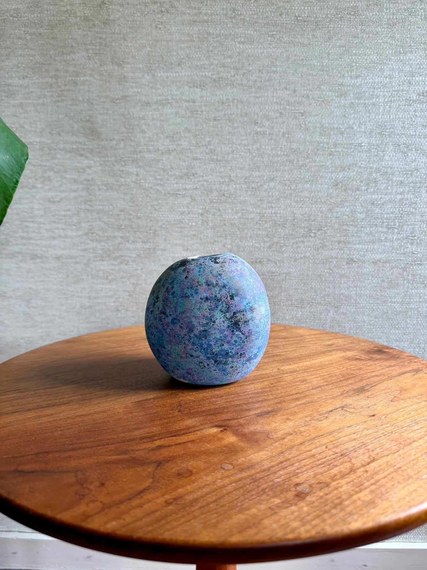 Blue speckled ball on a wooden surface with a gray textured wall background