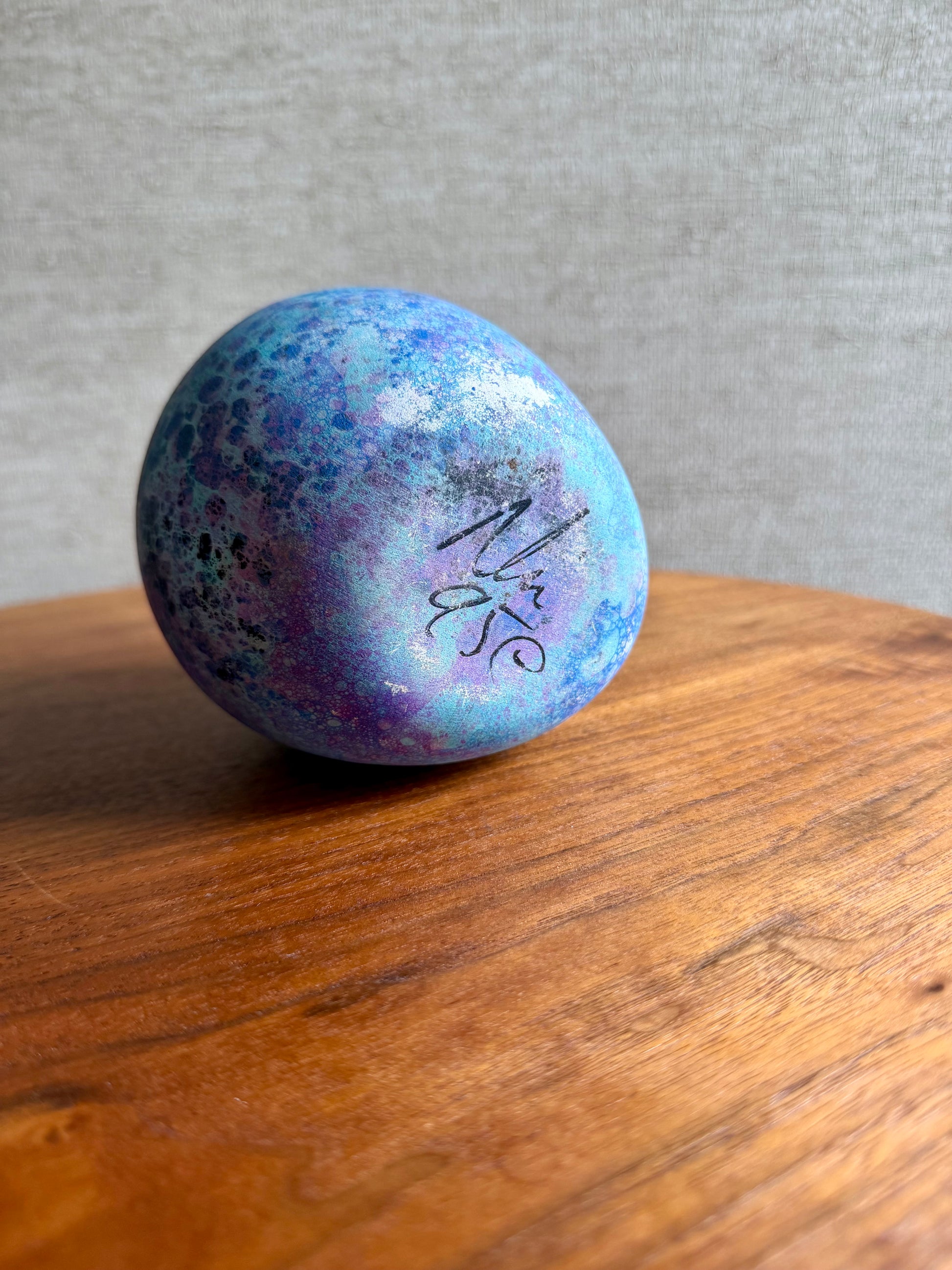 Blue and purple speckled ball on a wooden surface with a gray background