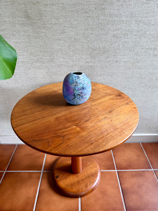 Wooden table with a ceramic vase on a tiled floor against a textured wall.