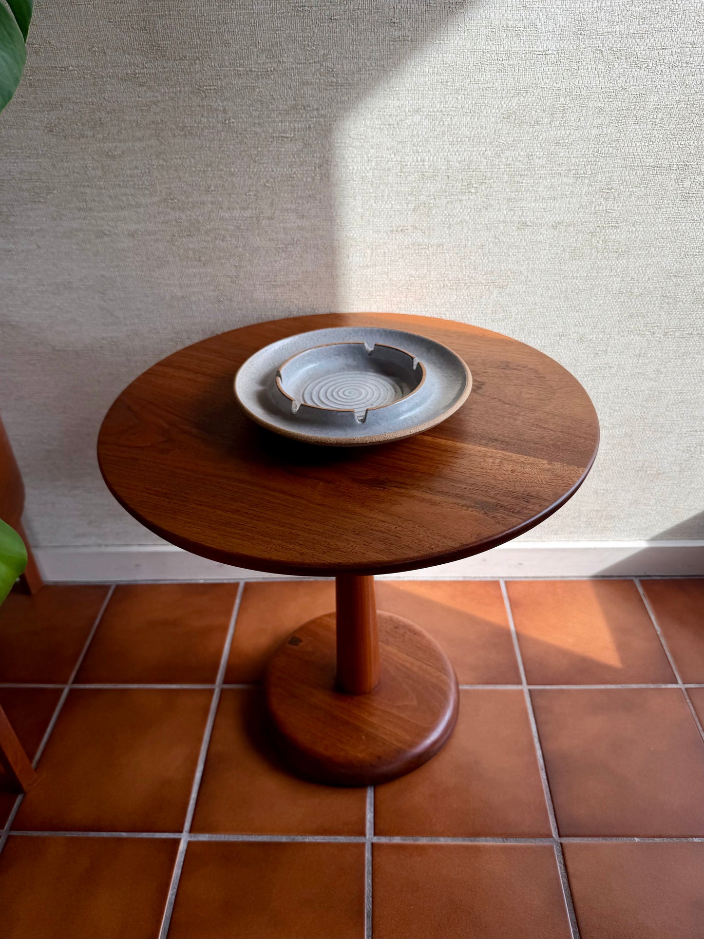Wooden side table with a ceramic ashtray on a tiled floor