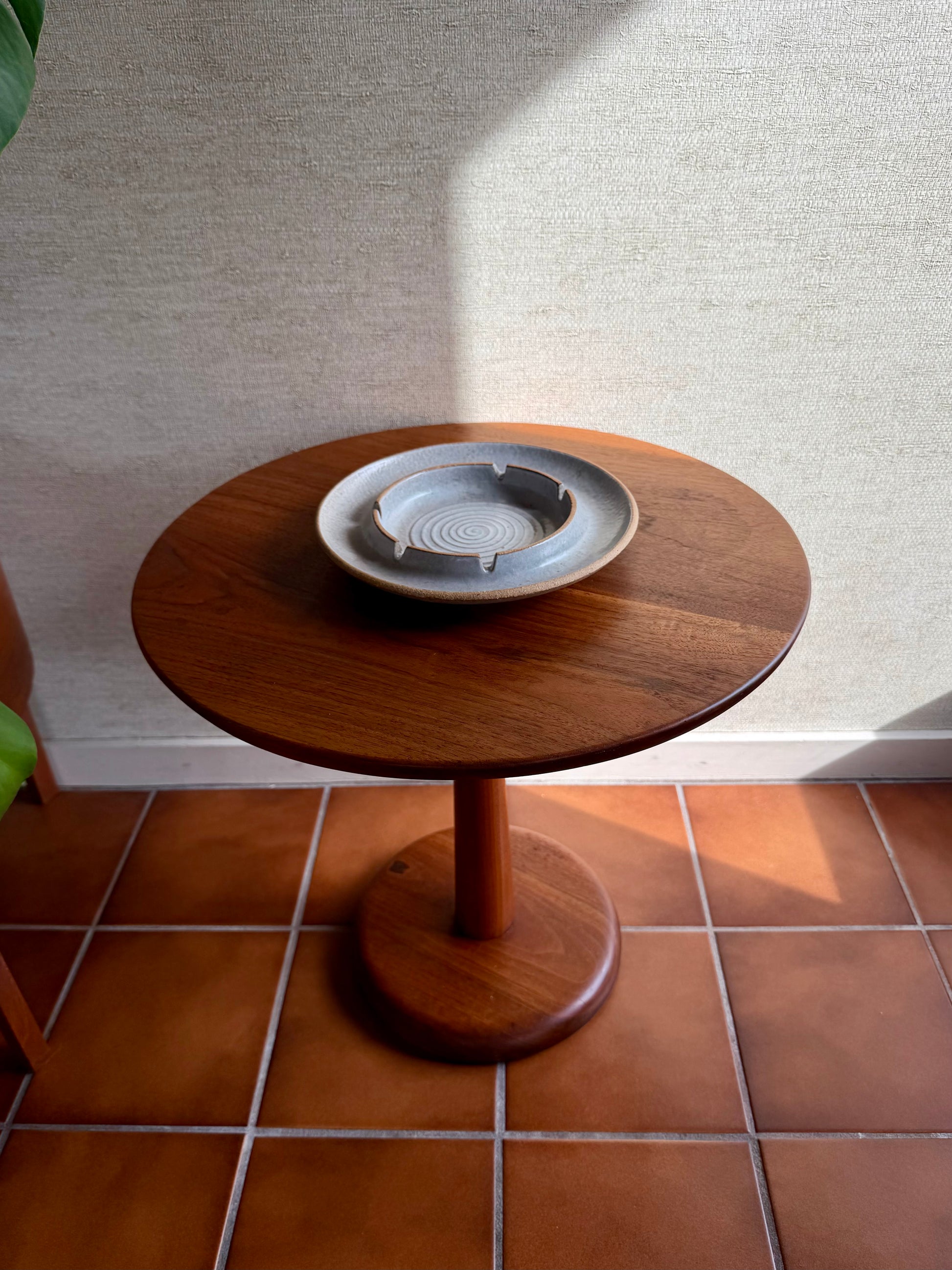 Wooden side table with a ceramic ashtray on a tiled floor