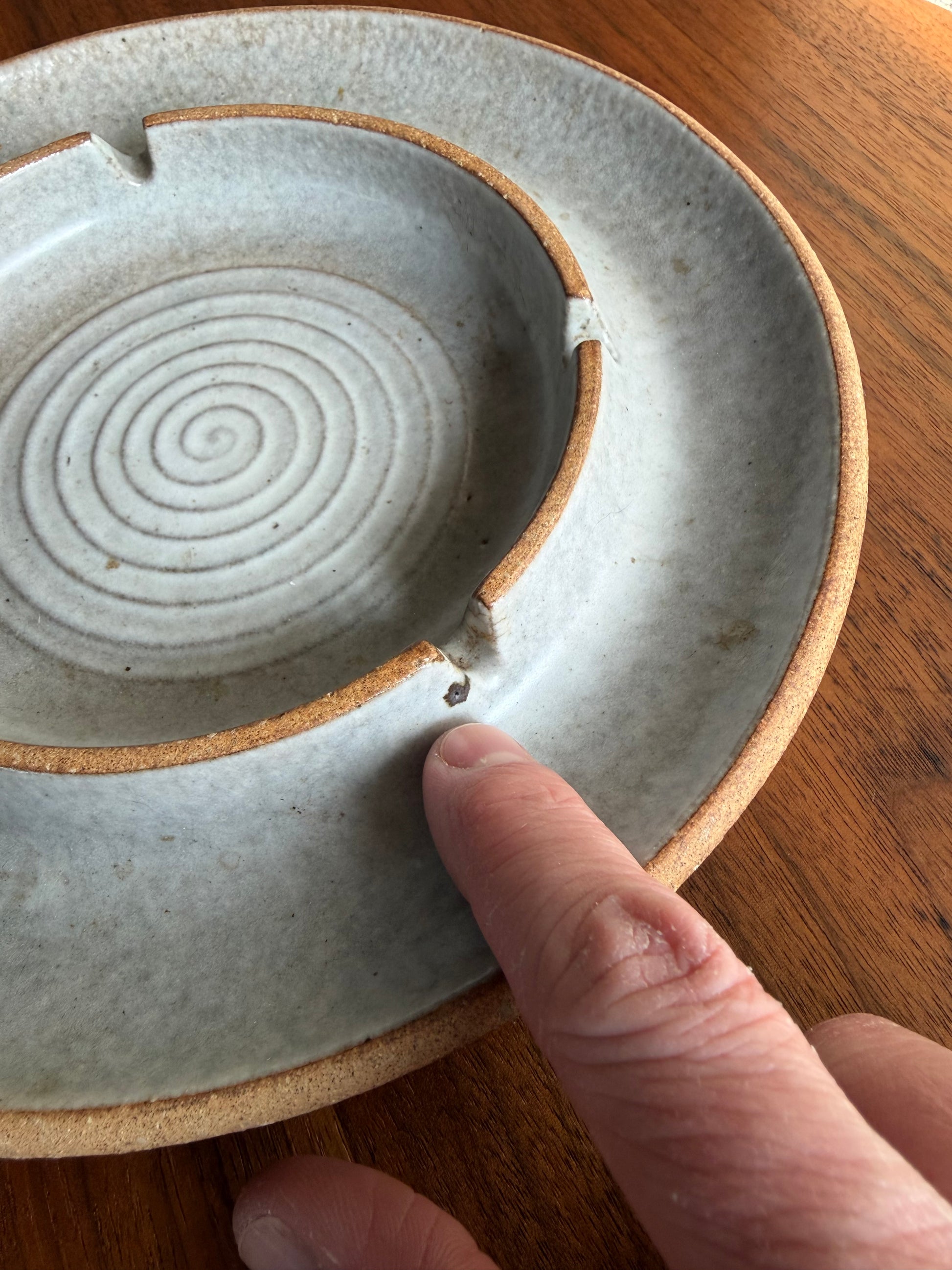 Ceramic dish with spiral design on a wooden surface, hand pointing to it