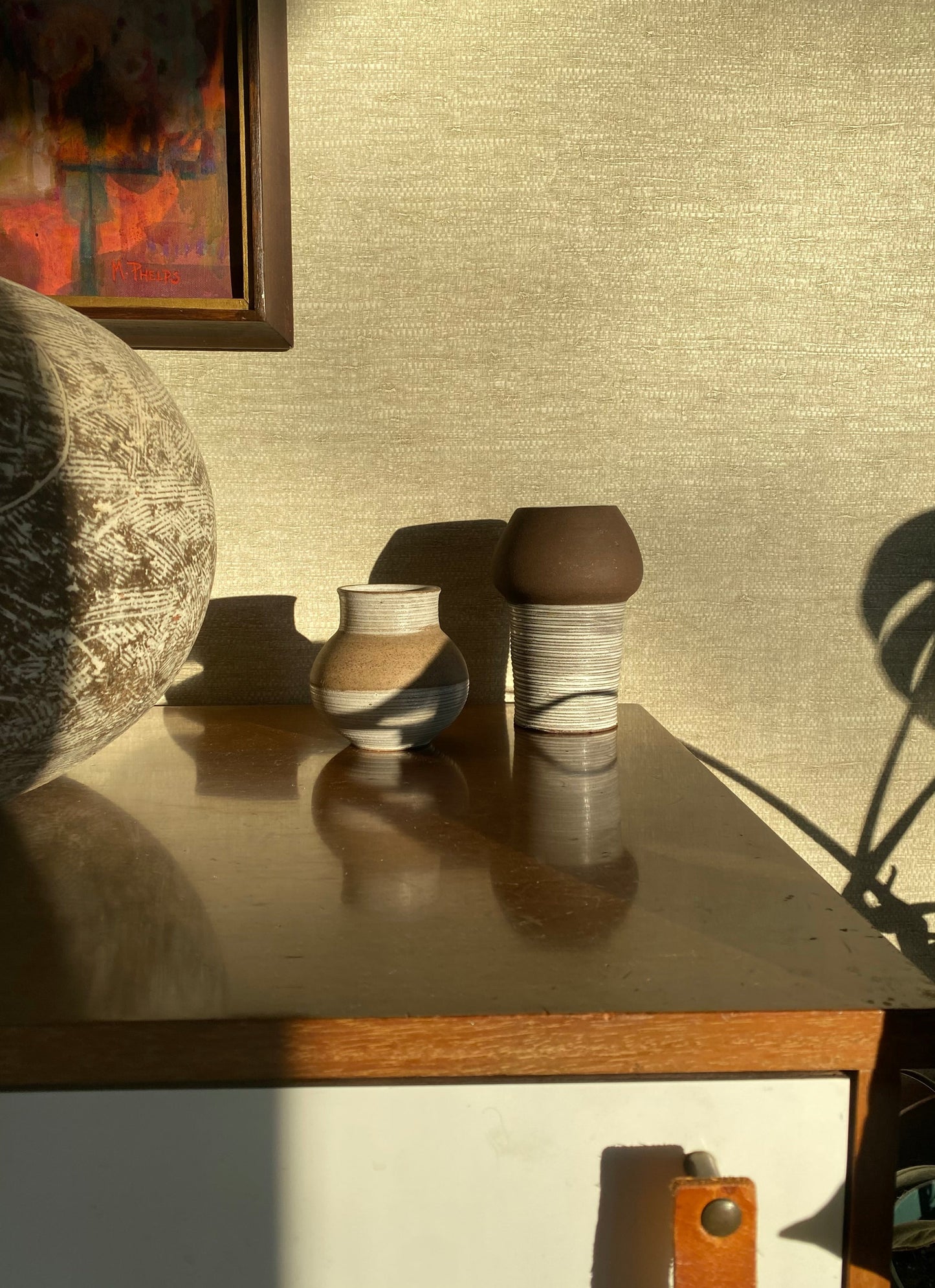 Two ceramic vases on a wooden surface with a textured wall in the background
