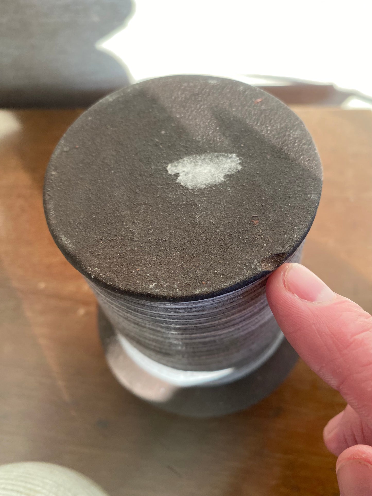 Close-up of a spool of thread with a hand holding it, on a wooden surface.