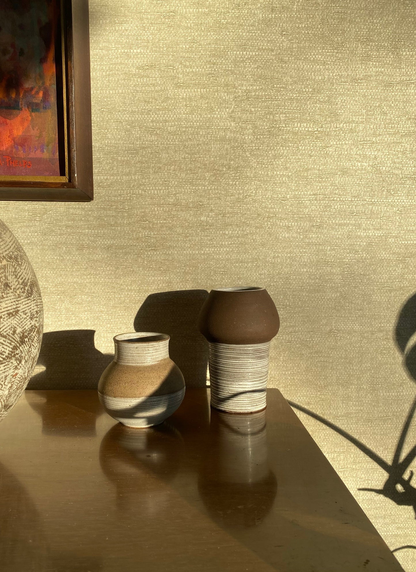 Two ceramic vases on a reflective surface with a textured wall in the background