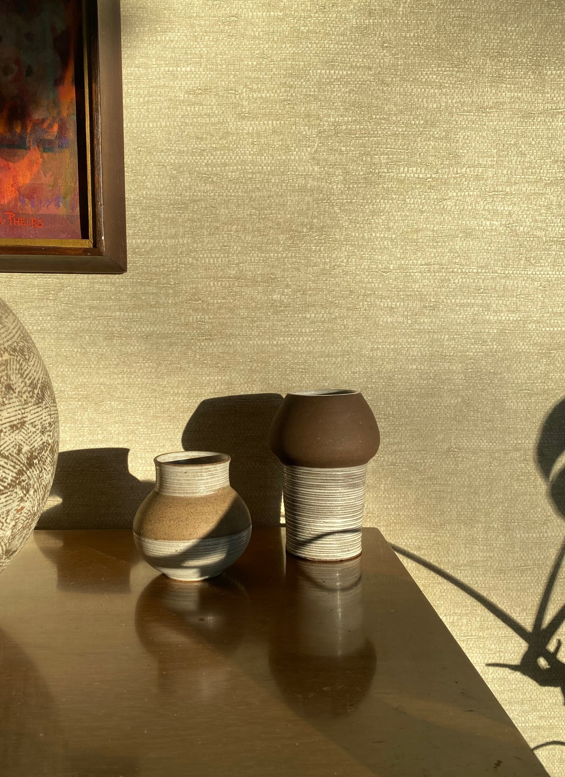 Two ceramic vases on a reflective surface with a textured wall in the background
