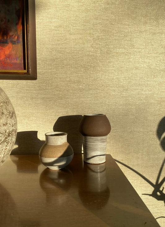 Two ceramic vases on a reflective surface with a textured wall in the background