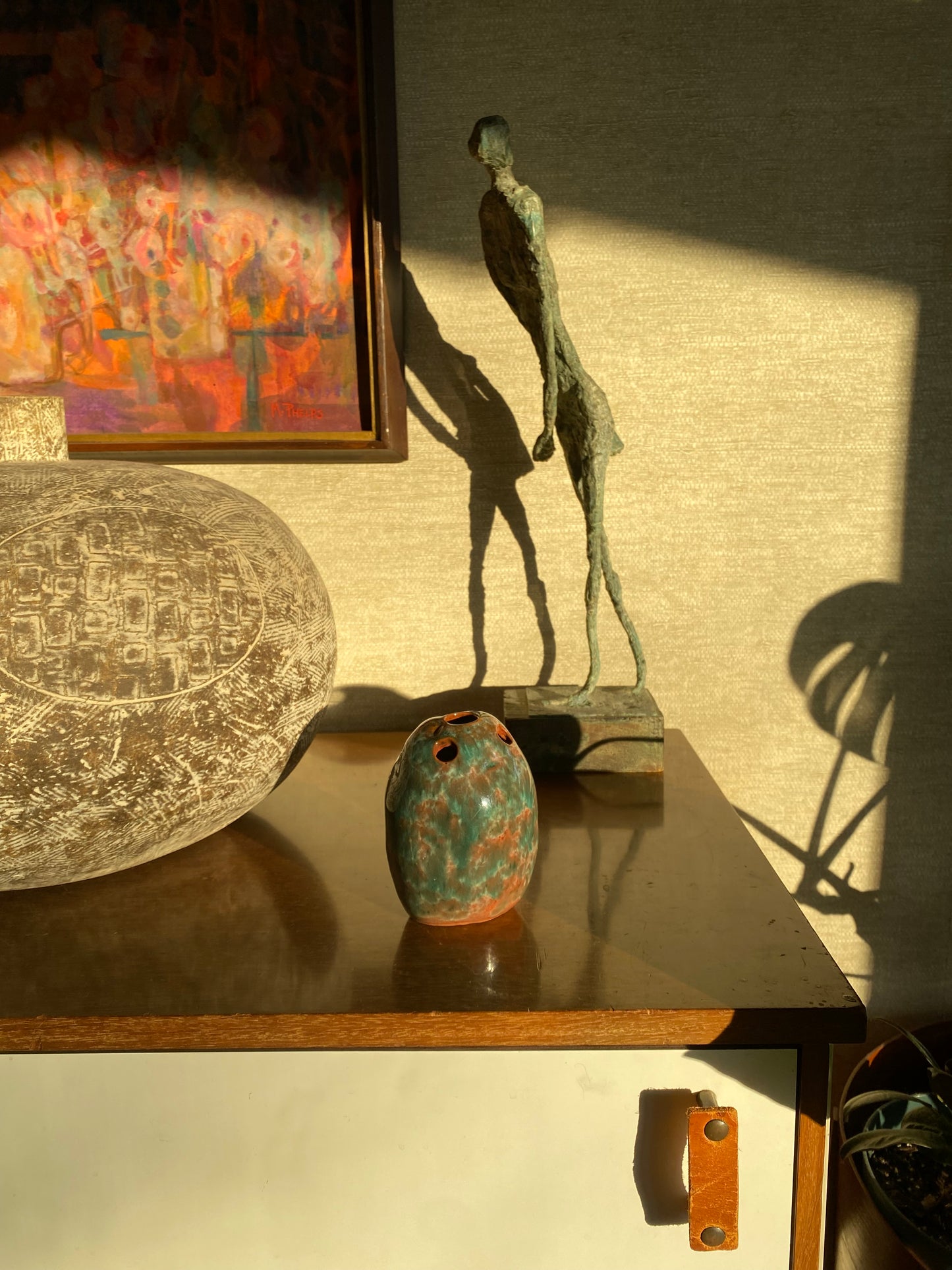 Abstract sculpture on a textured surface with a framed artwork and decorative object in the background.