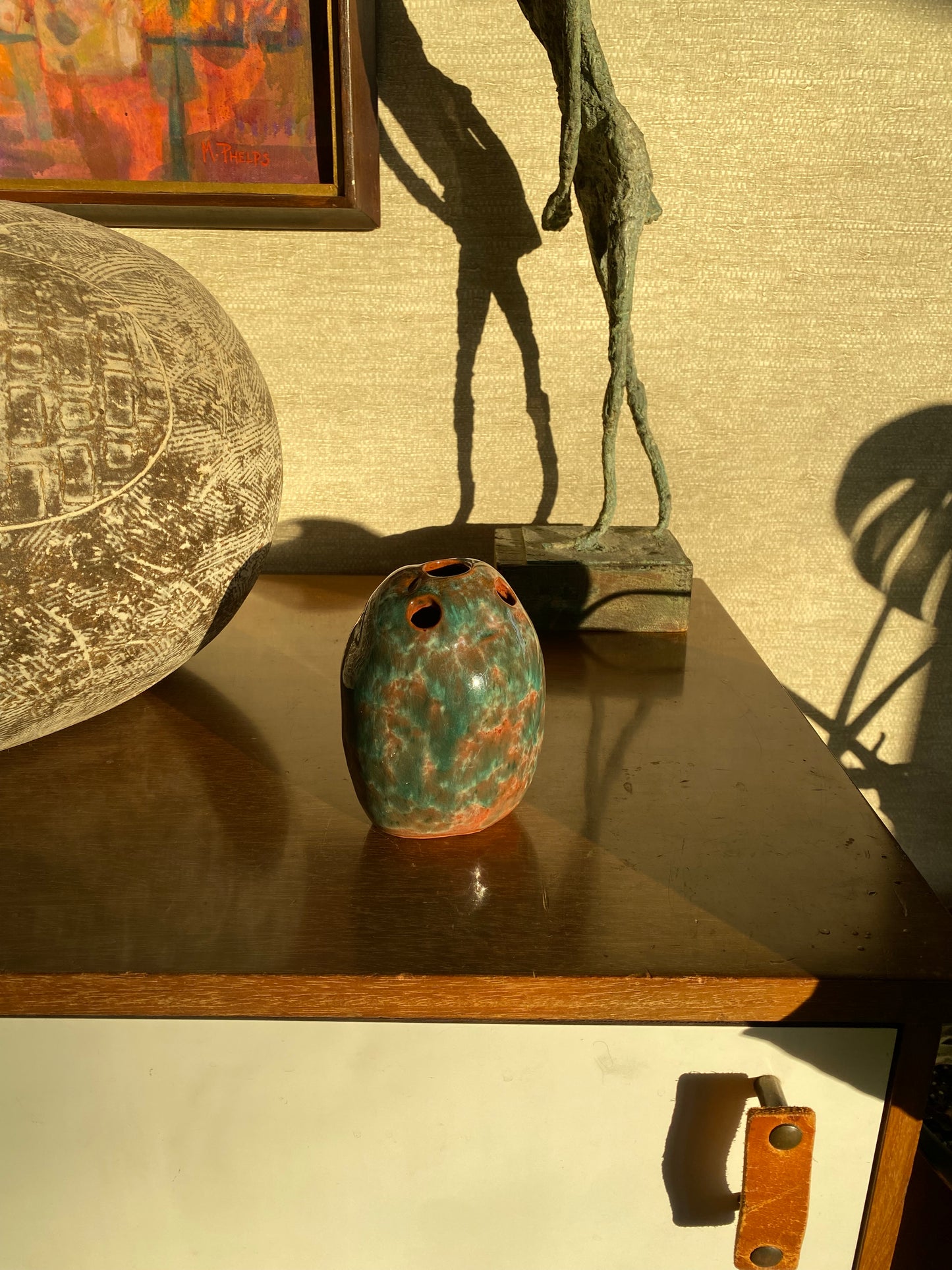 Decorative objects including a textured sphere and a greenish-brown vase against a textured wall.