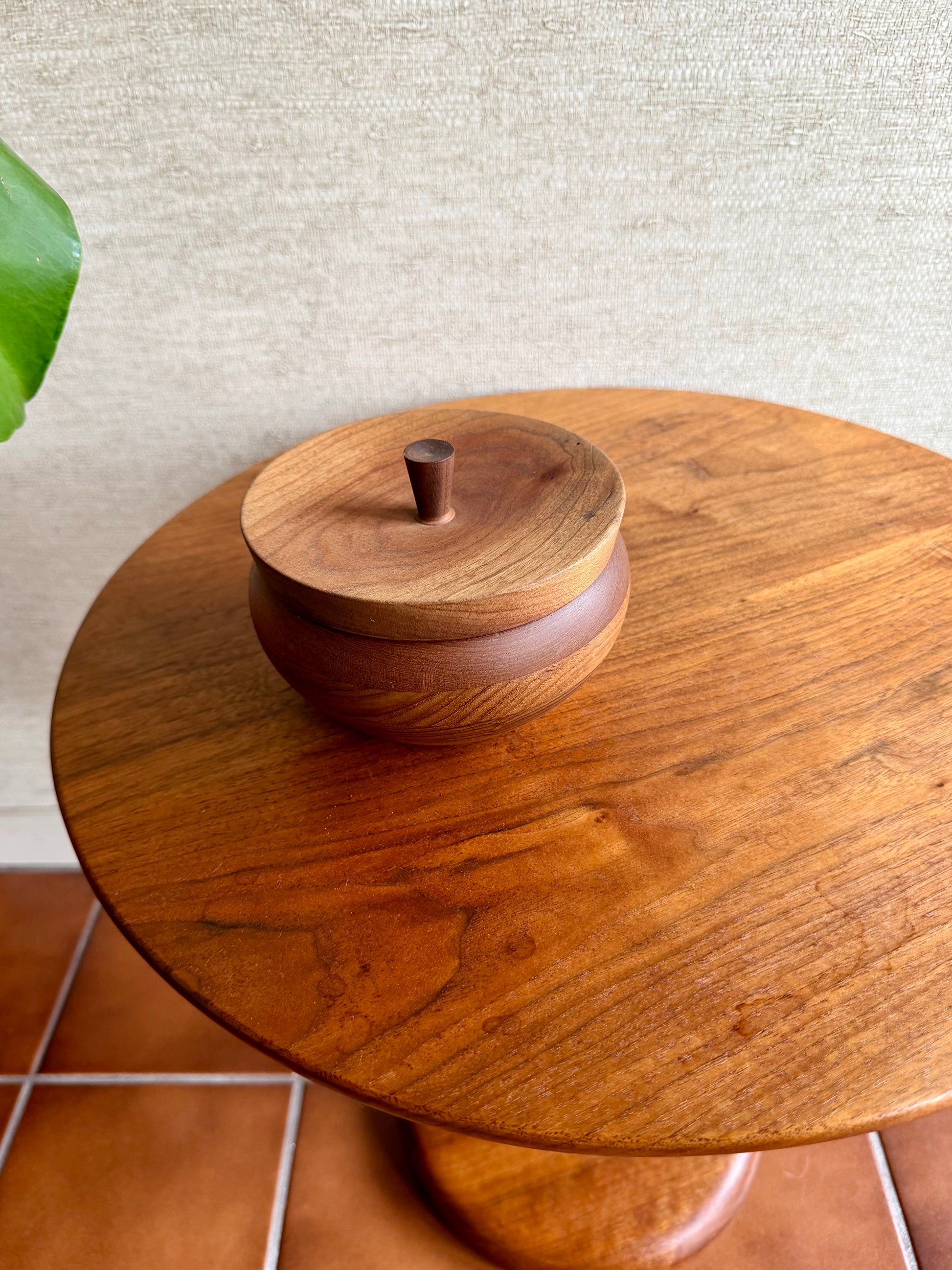 Wooden container with a lid on a wooden table against a textured wall.