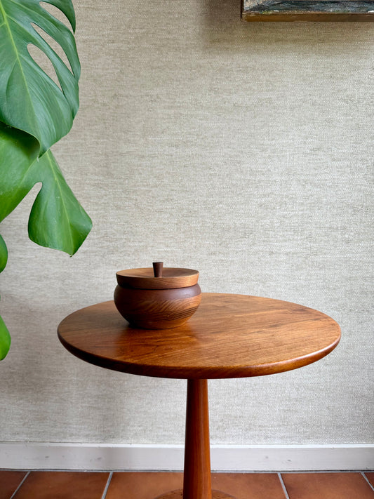 Wooden side table with a decorative bowl against a textured wall.