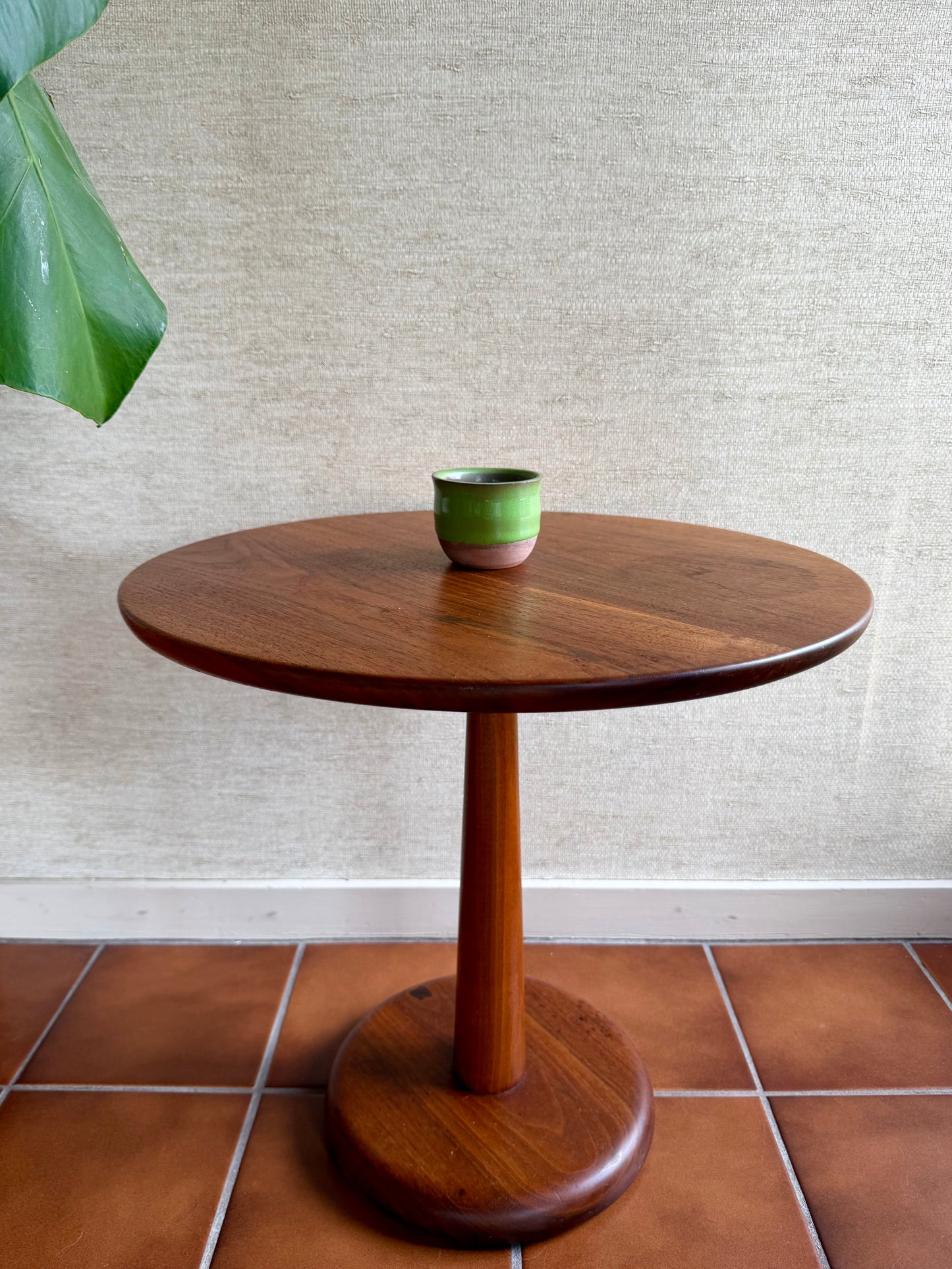 Wooden side table with a green ceramic cup on a textured wall and tiled floor background